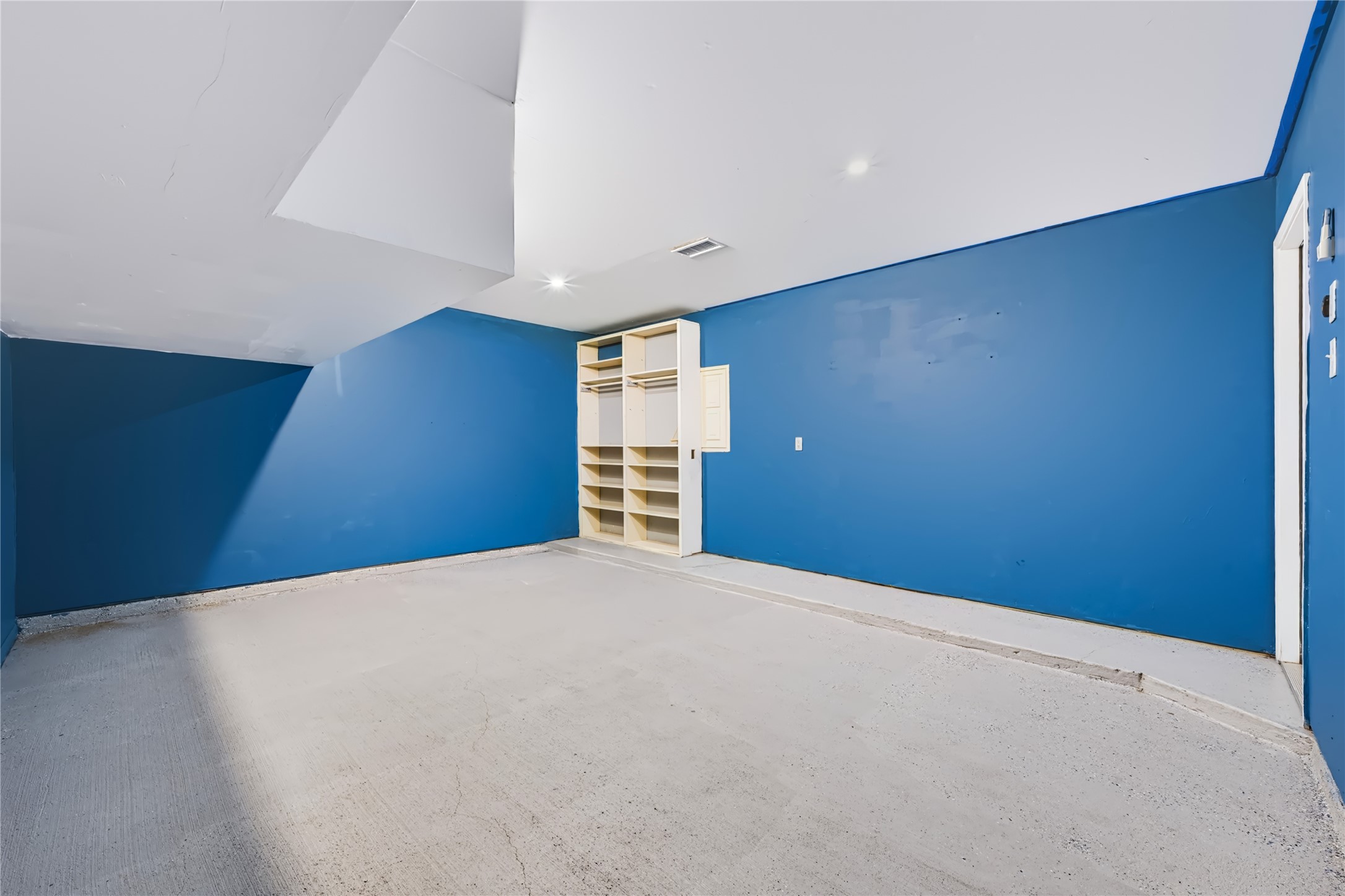 Versatile extra room featuring bold blue accent walls, built-in storage cabinets, and a private mini-split AC unitideal for use as a game room, media room, or extra bedroom