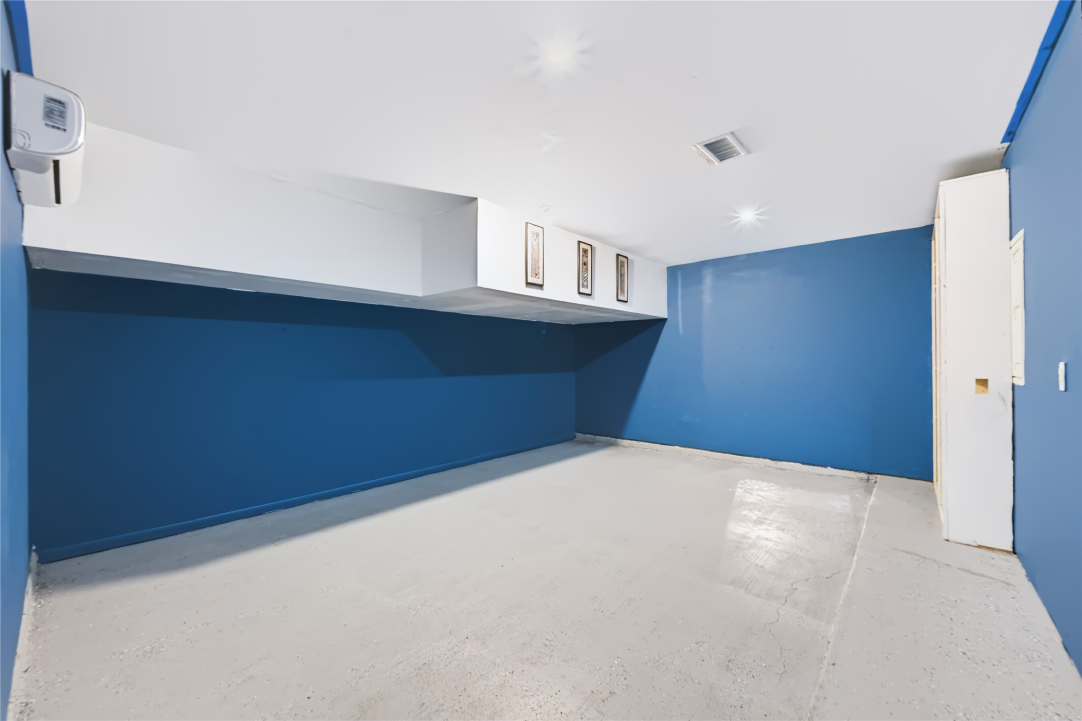 Versatile extra room featuring bold blue accent walls, built-in storage cabinets, and a private mini-split AC unitideal for use as a game room, media room, or extra bedroom