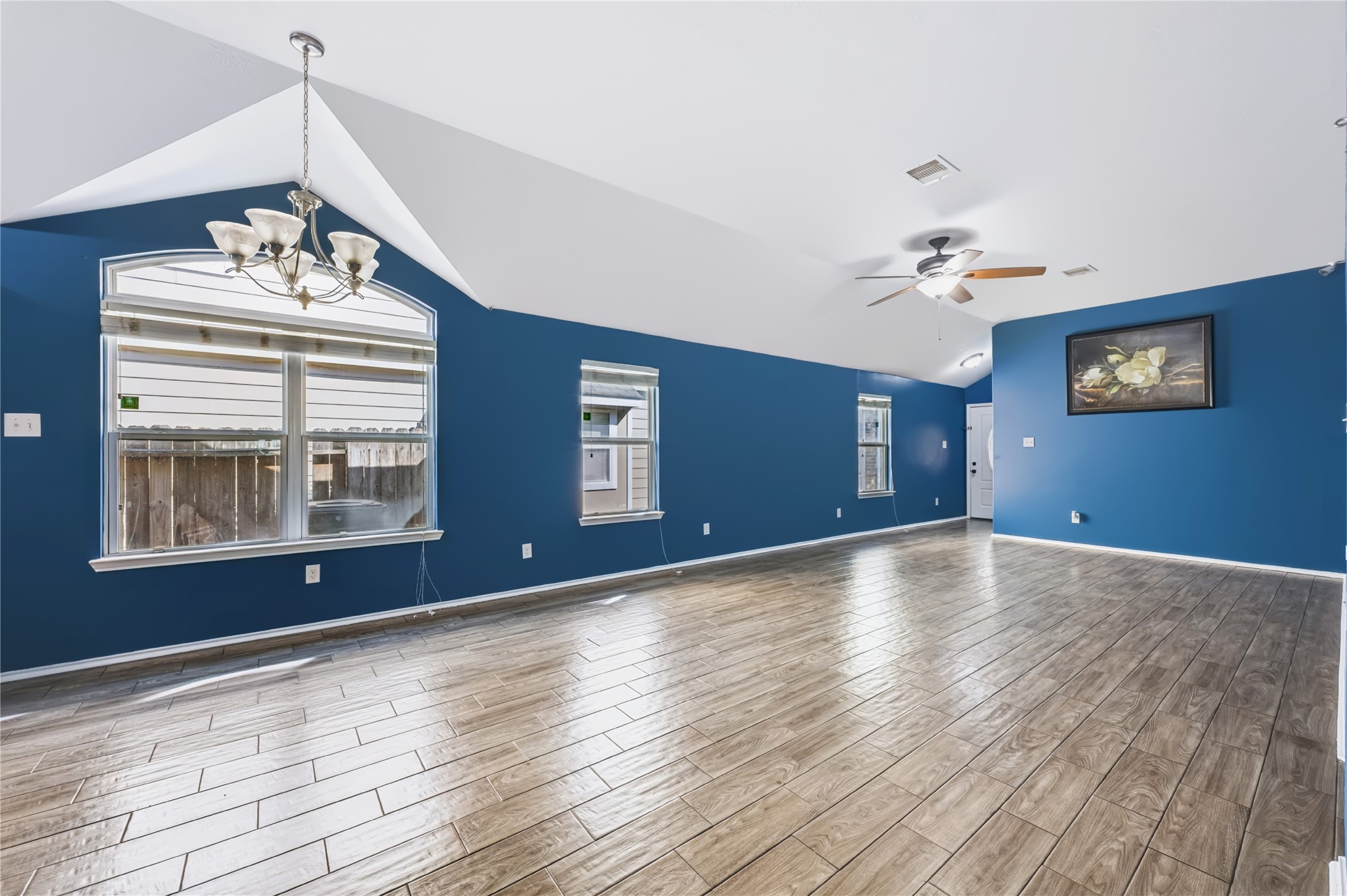 Spacious open-concept living area featuring rich wood-look tile flooring, vaulted ceilings, a modern ceiling fan, and vibrant accent walls. Spacious open-concept living area featuring rich wood-look tile flooring, vaulted ceilings, a modern ceiling fan, and vibrant accent walls.
