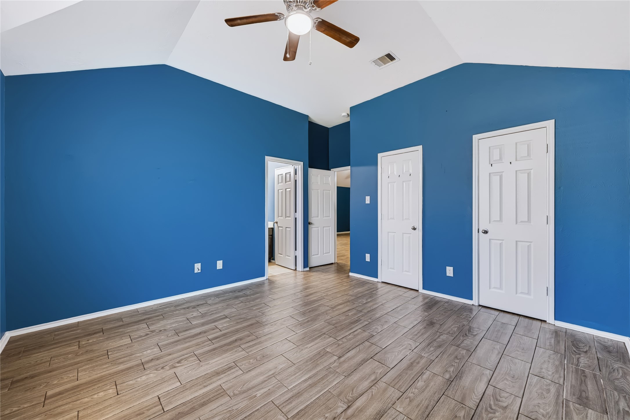 Spacious master bedroom featuring high vaulted ceilings, rich wood-look tile flooring, an upgraded ceiling fan, and large windows bringing in plenty of natural light.