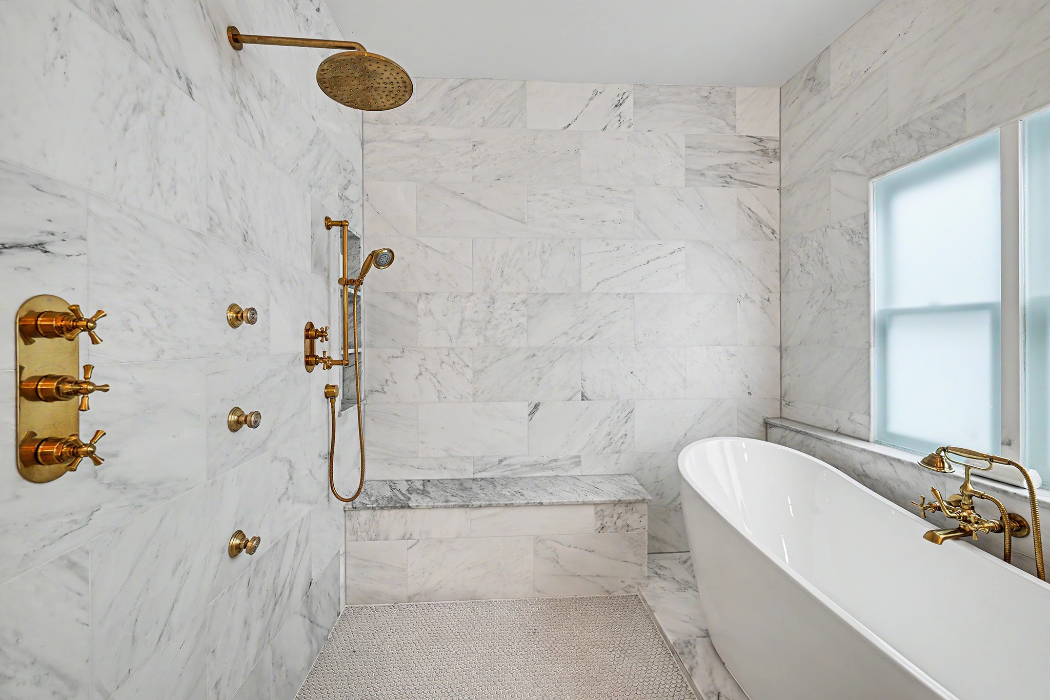 Shower includes dual showerheads and body sprays. Bench seat in place as well. Freestanding tub with dazzling faucet is surrounded by marble tile.