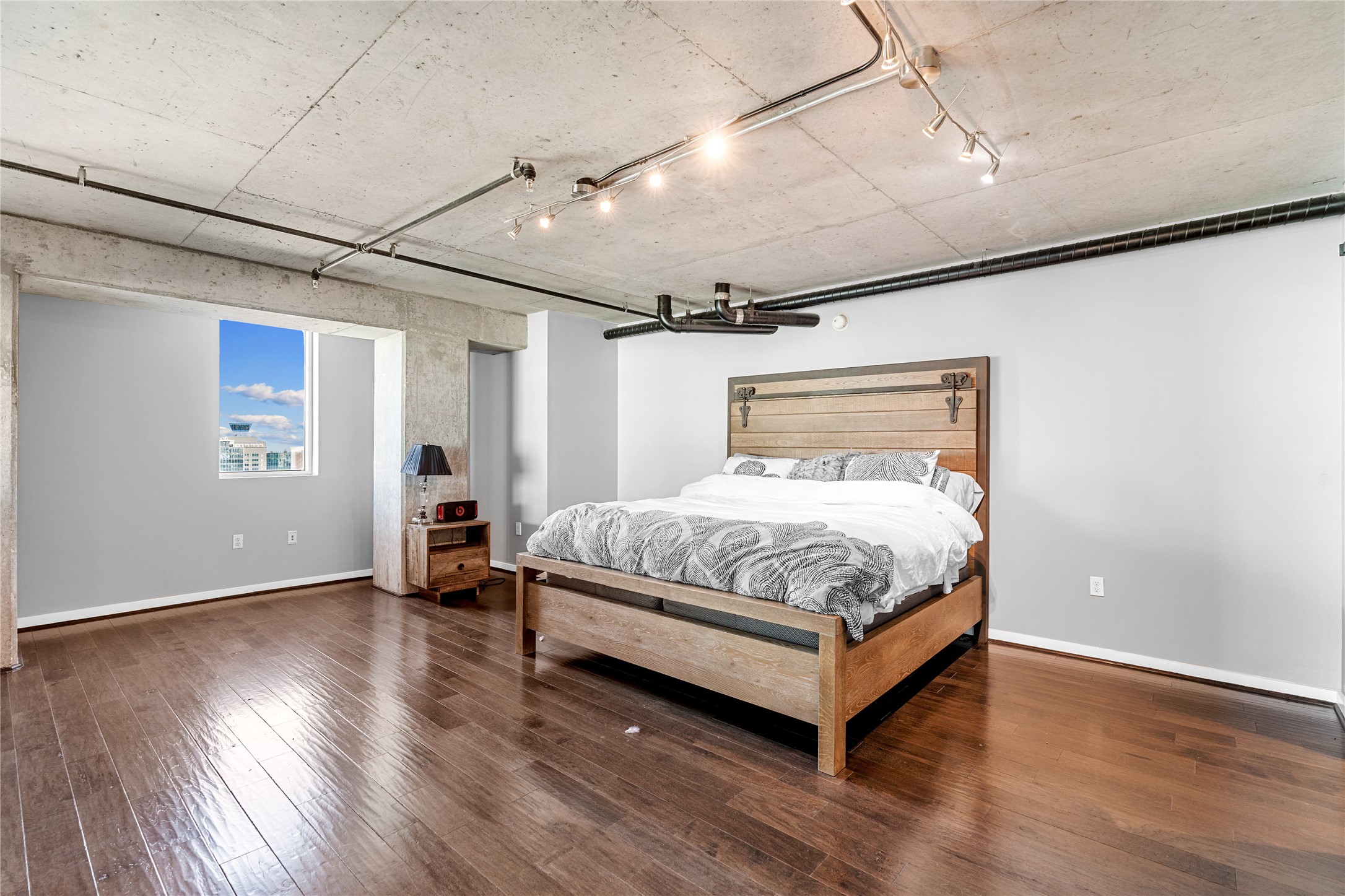 Another perspective of the expansive primary suite highlights generous proportions, warm wood flooring and exposed concrete ceilings, leaving ample room for a private sitting area.