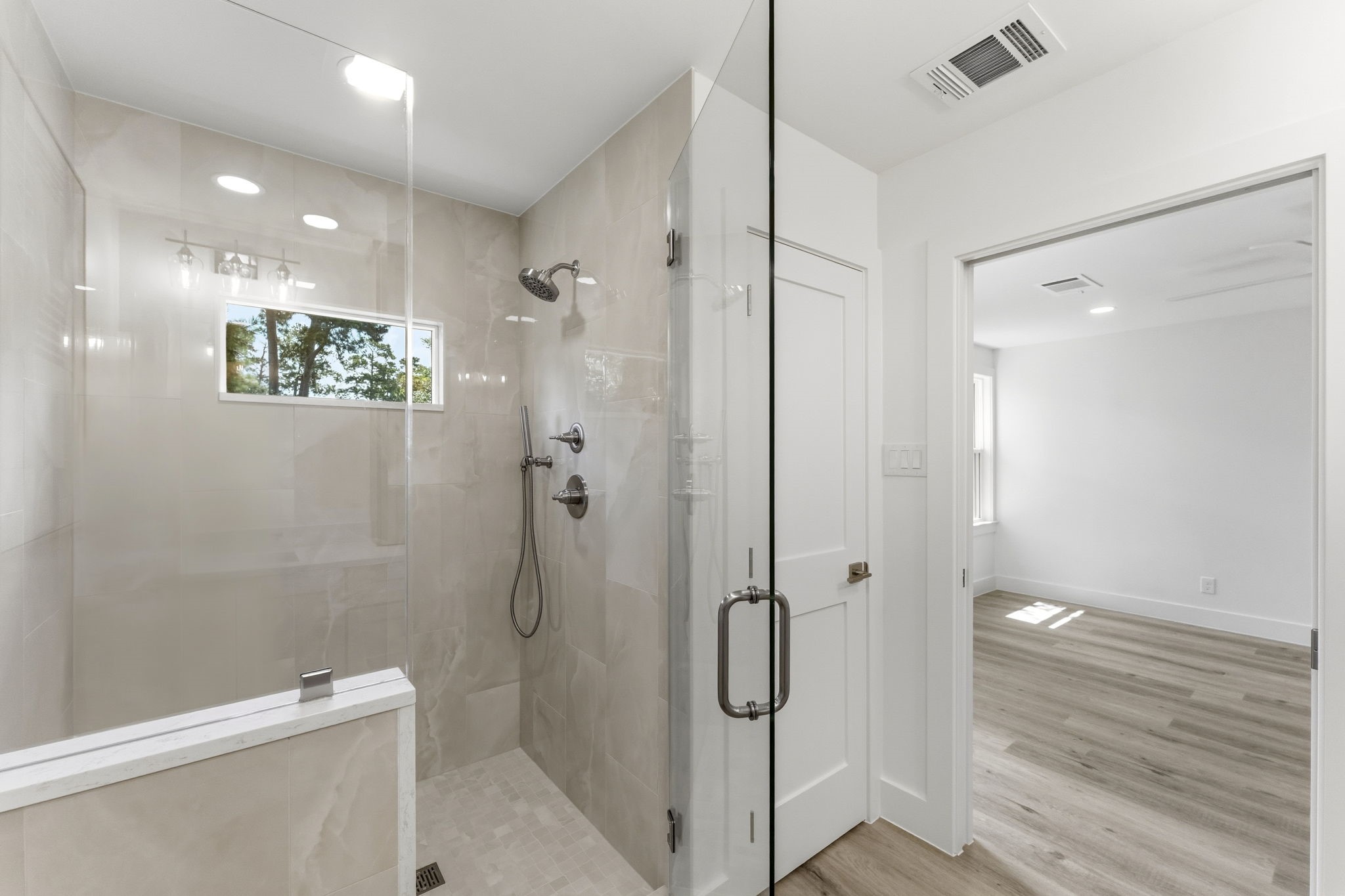 The luxurious primary  features a spacious frameless glass walk-in shower beautifully finished with designer tile extending to the ceiling.