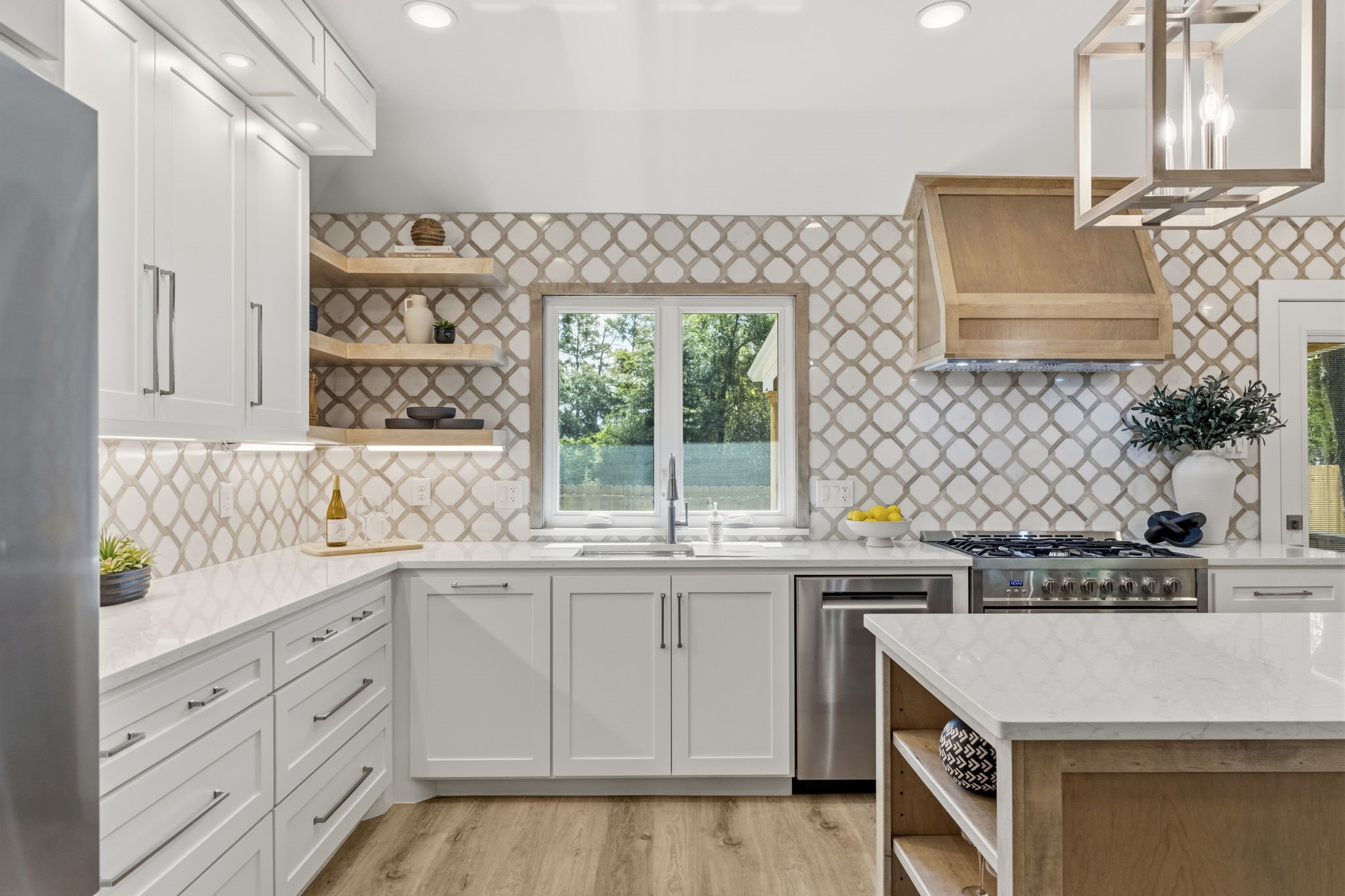 The handcrafted full-height tile backsplash serves as a stunning focal point, complemented by custom shaker cabinetry with soft-close doors and drawers, under-cabinet lighting, quartz countertops, and warm wood shelving