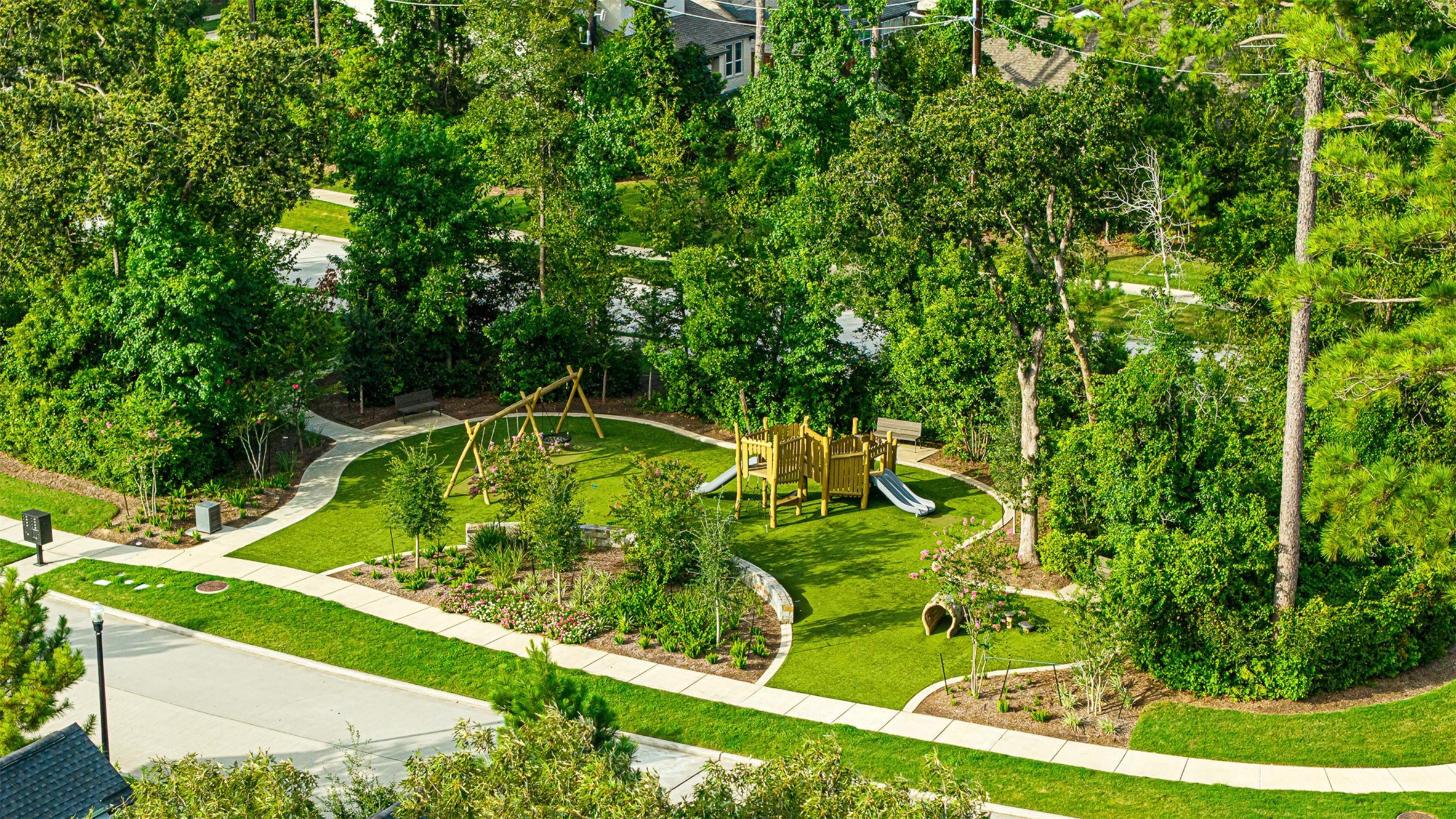 Tucked amidst lush greenery, the community playground features wooden play structures, swings, and manicured turf surrounded by winding paved walking paths.