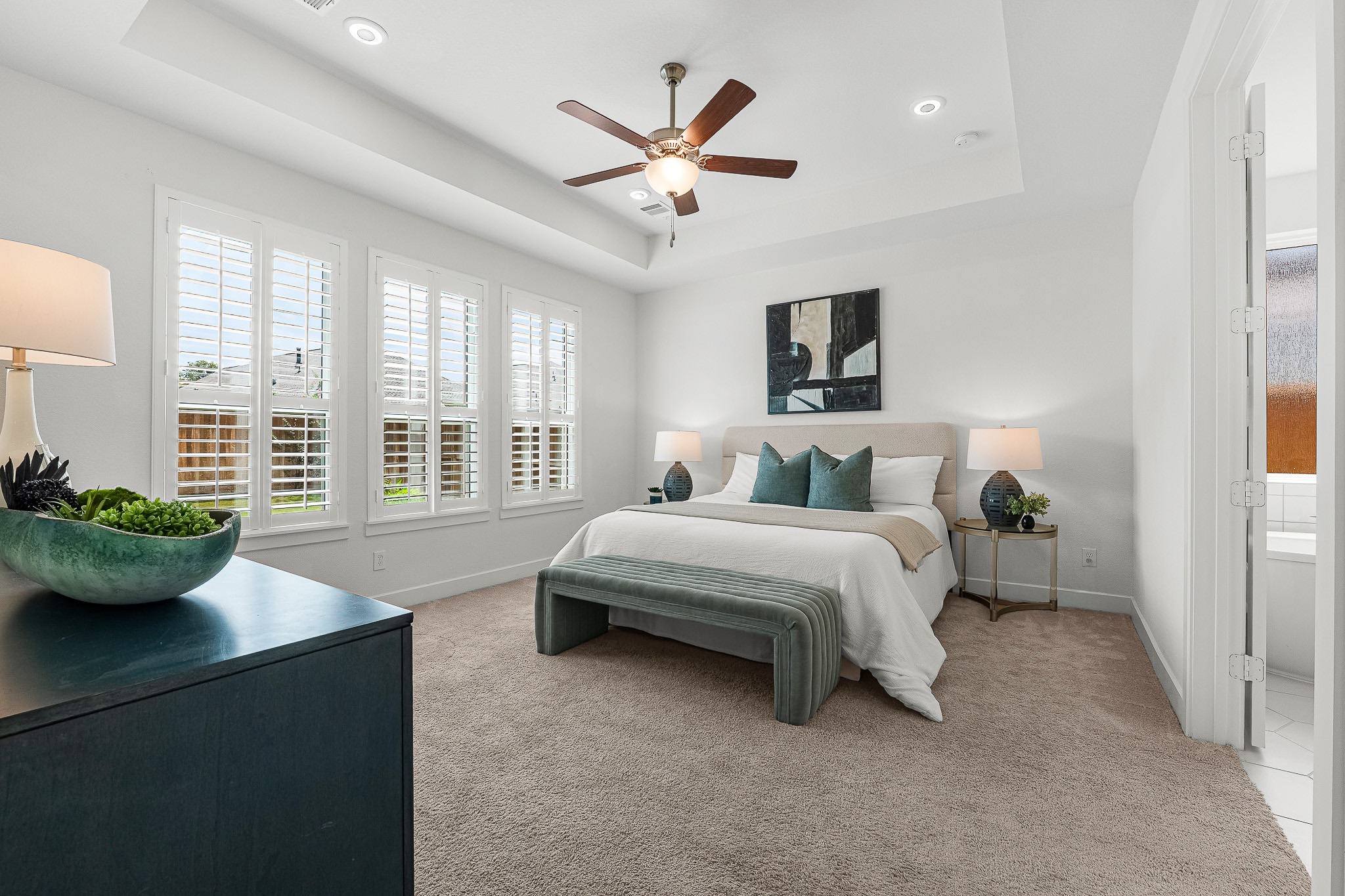 High tray ceilings and classic plantation shutters enhance the spacious first-floor primary suite. Soft neutral carpeting and direct access to the private ensuite bath create a serene sanctuary designed for rest.