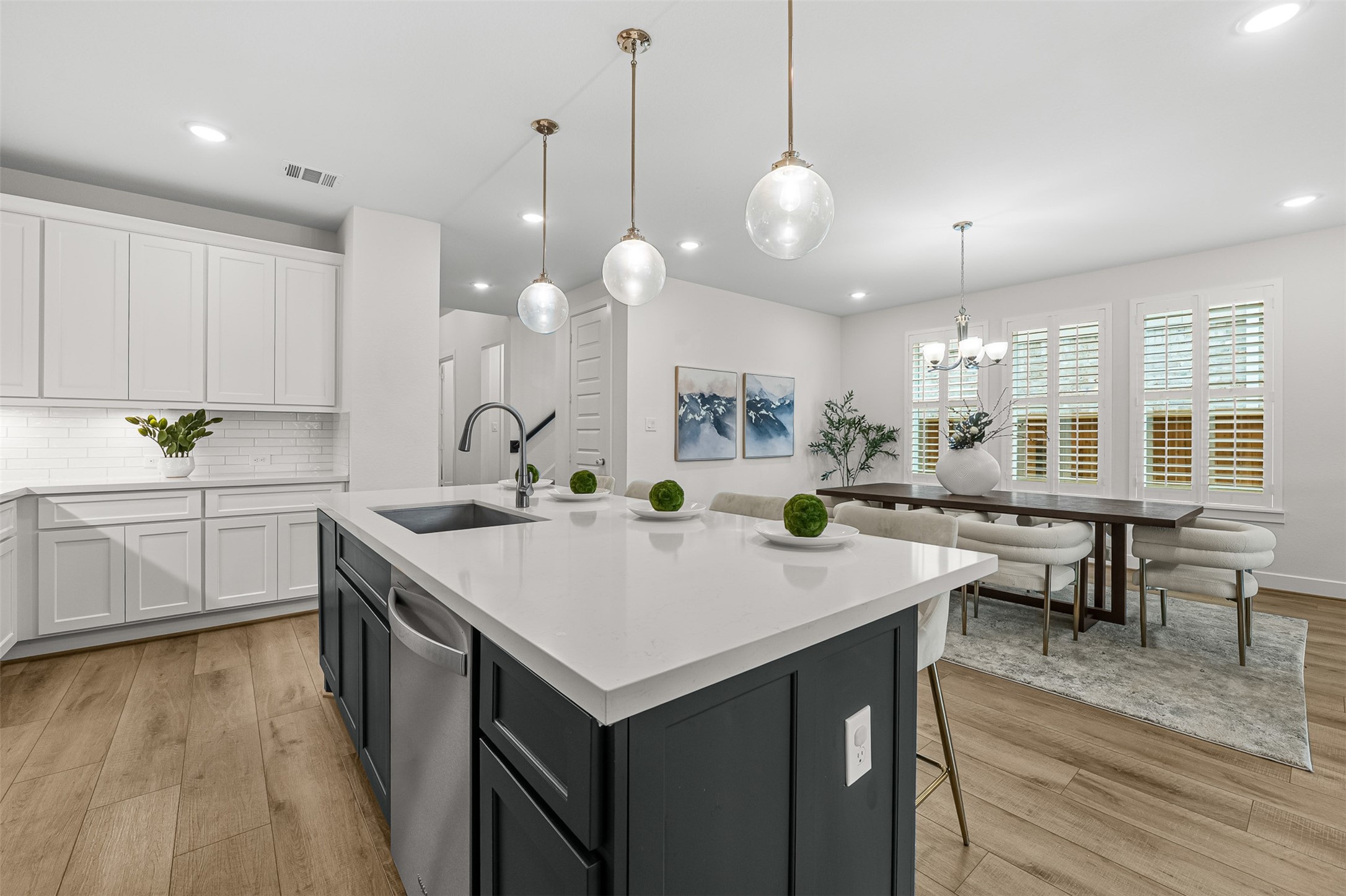 Stylish pendant lights illuminate an oversized contrast island topped with quartz counters, seamless to the nearby dining nook. Clean white cabinetry, stainless steel appliances, and a subway tile backsplash complete this gourmet kitchen layout.