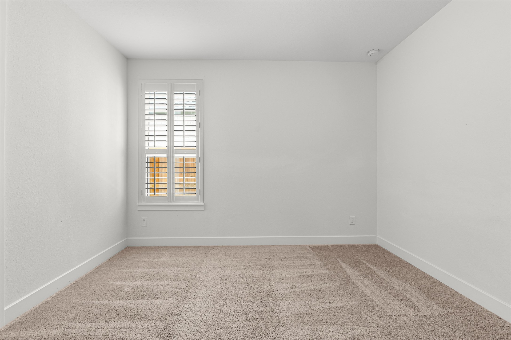 Soft carpet flooring and crisp plantation shutters define this secondary bedroom, offering a clean neutral palette for guests or personalized decor.