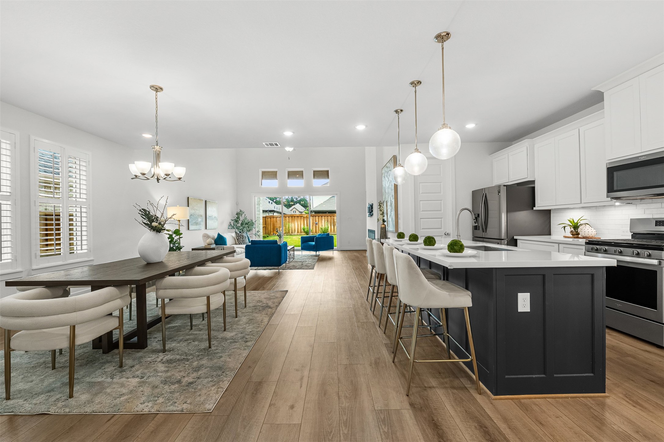 Expansive open-concept main floor features seamless flow between the formal dining area, gourmet kitchen, and sunlit living room with high ceilings. An oversized navy contrast island with quartz countertops anchors the space, illuminated by modern pendant lighting and complemented by wood-look flooring.