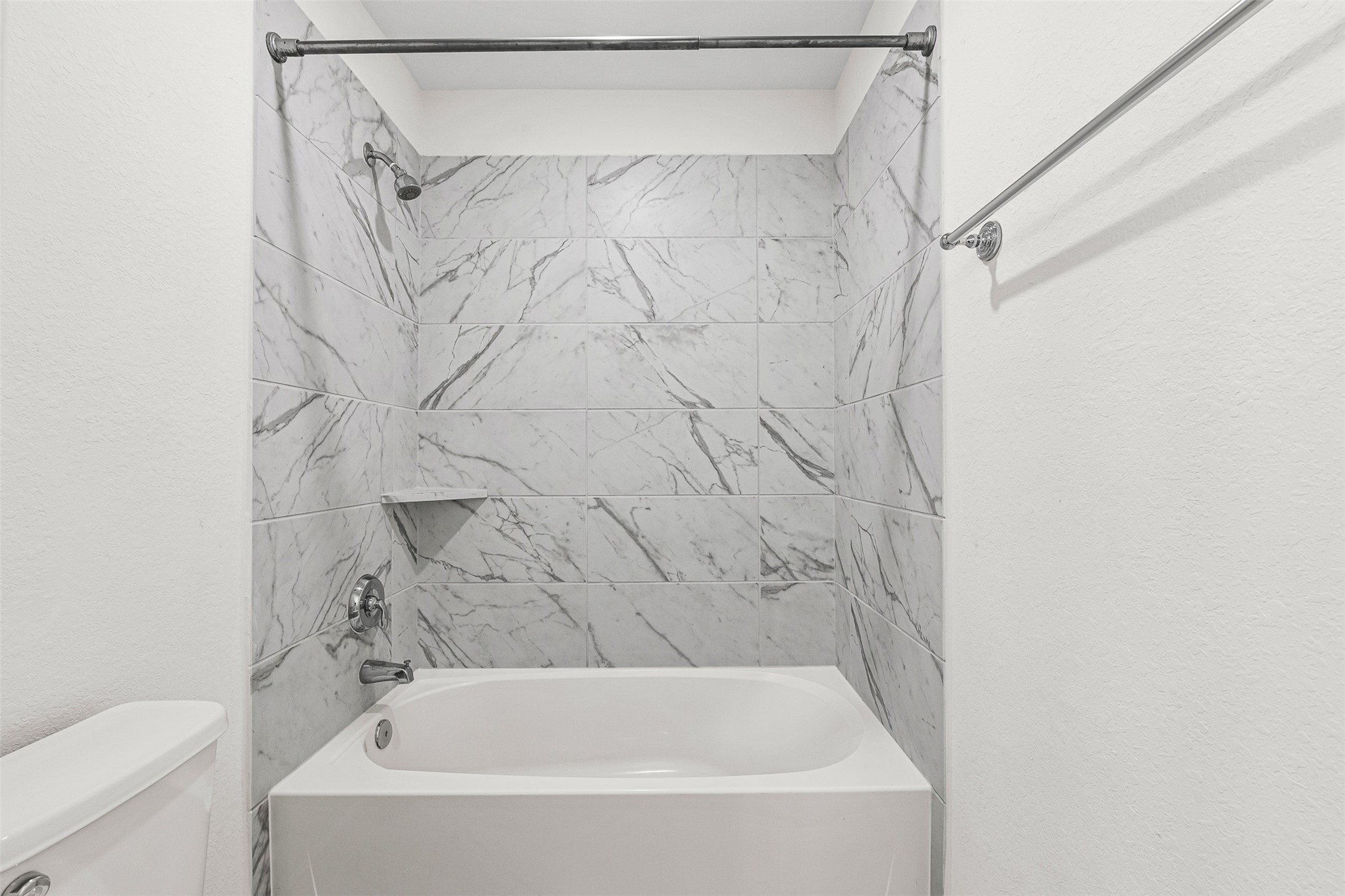Luxurious floor-to-ceiling marble-patterned tile surrounds this soaking tub and shower combination, bringing a sleek spa aesthetic to the bathroom. Modern chrome fixtures and a built-in display shelf complete the elegant, light-filled space.