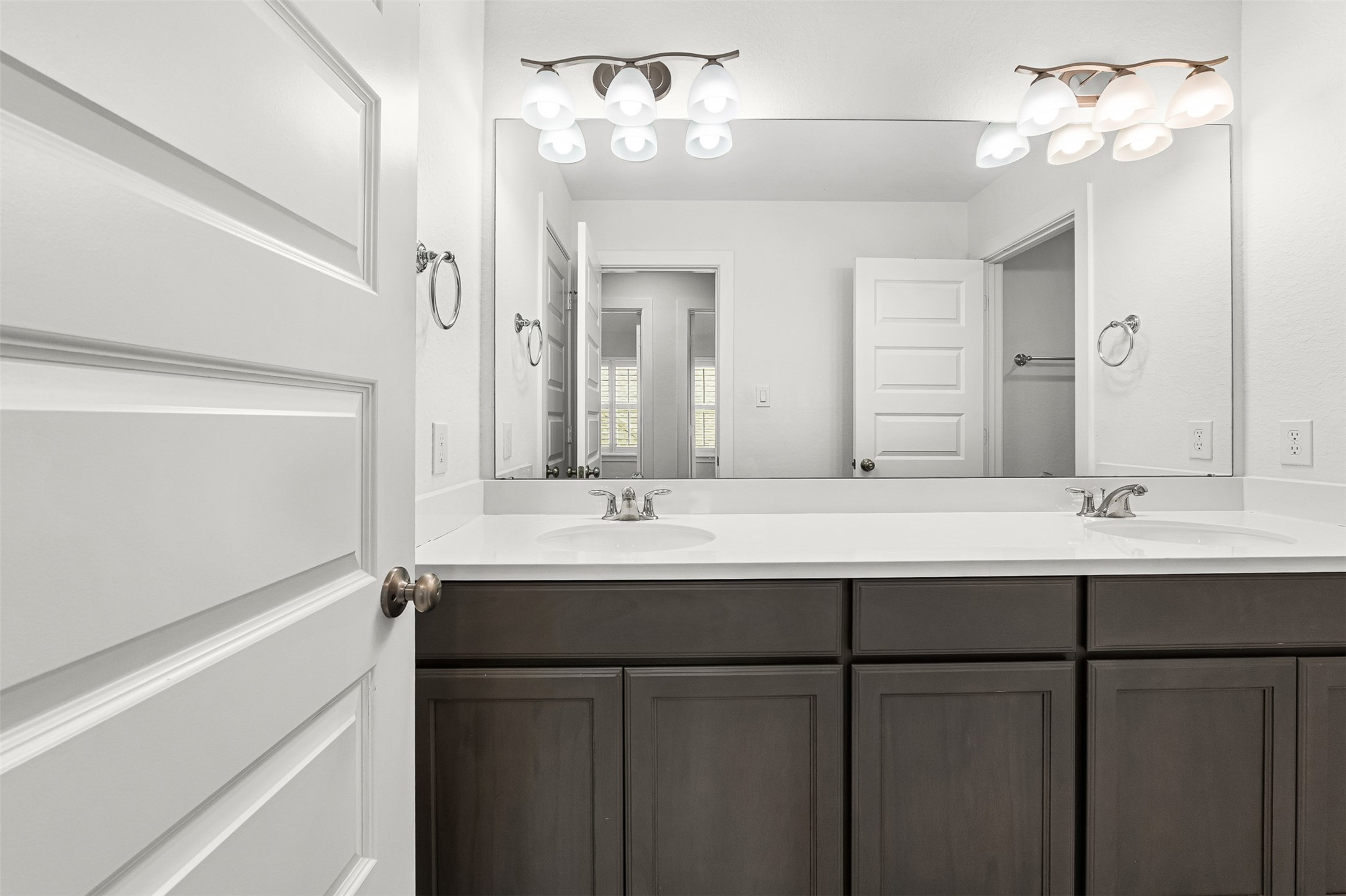 A dark contrast vanity with dual sinks and white quartz countertops creates a striking focal point in this secondary full bathroom. Modern multi-light sconces, a full-width mirror, and classic brushed nickel hardware complete the sleek, organized design.