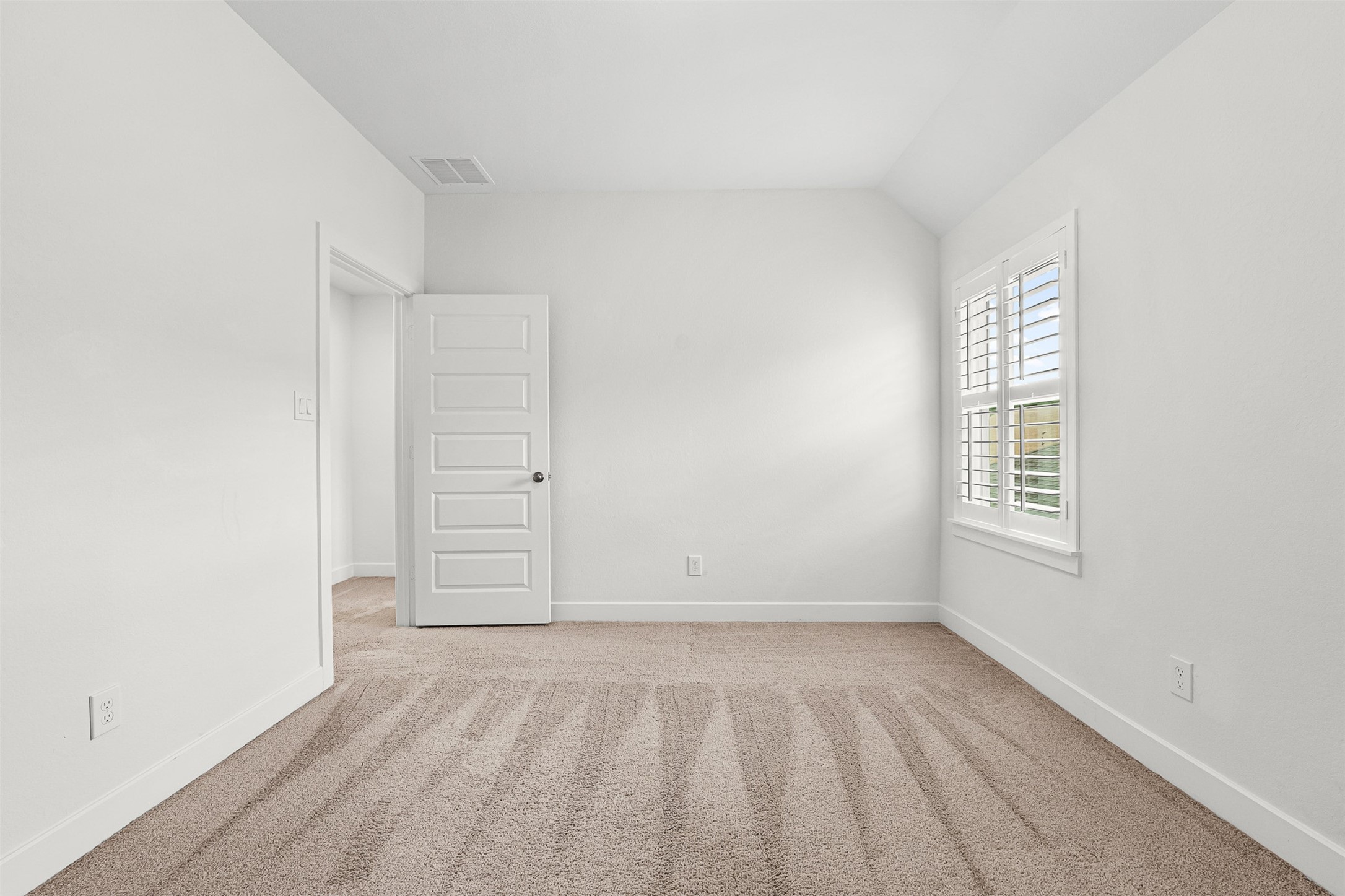 Crisp plantation shutters frame the window in this secondary bedroom, featuring soft carpet flooring and classic neutral walls. Sloped ceiling accents add architectural depth to the versatile layout.