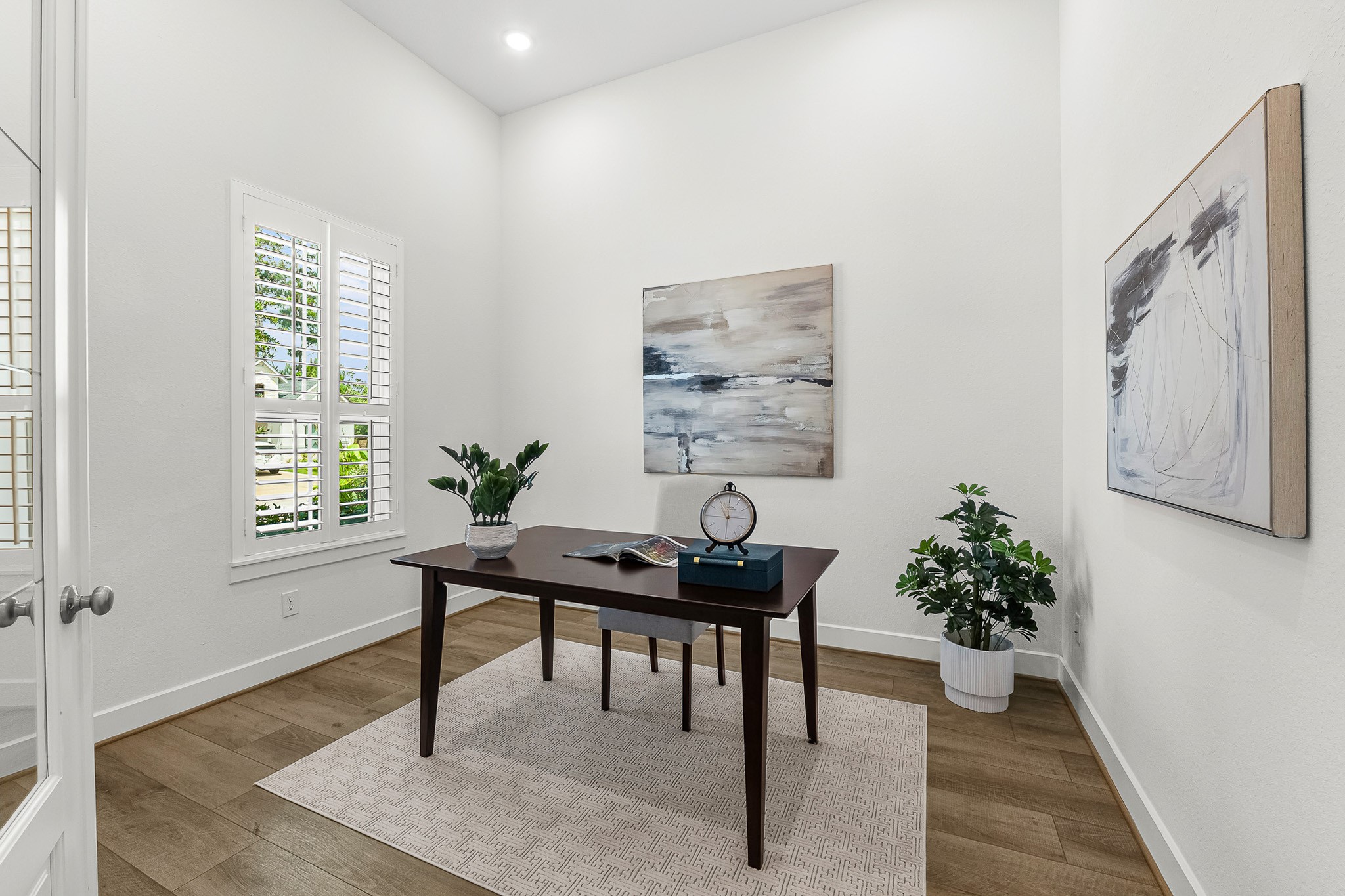 Tucked behind elegant French doors, this private study features crisp plantation shutters, warm wood-look floors, and soaring ceilings. Thoughtfully positioned on the main level, the light-filled space provides a serene, quiet atmosphere for remote work or study.