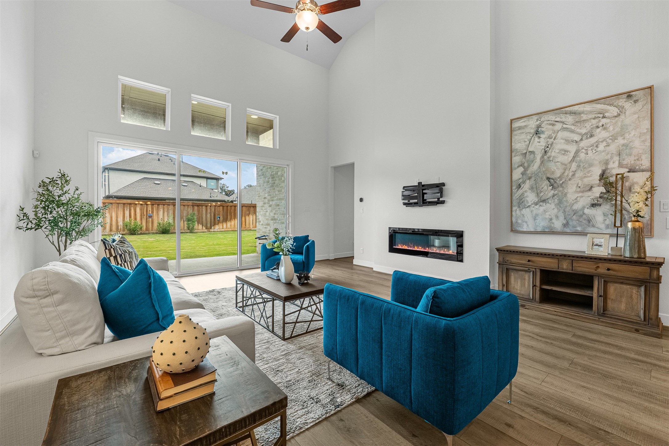 Framed by soaring double-height ceilings, this spacious living room features a sleek linear fireplace and wood-look plank floors. Sliding glass doors and transom windows bring in natural light while opening directly to the private covered patio and green yard.
