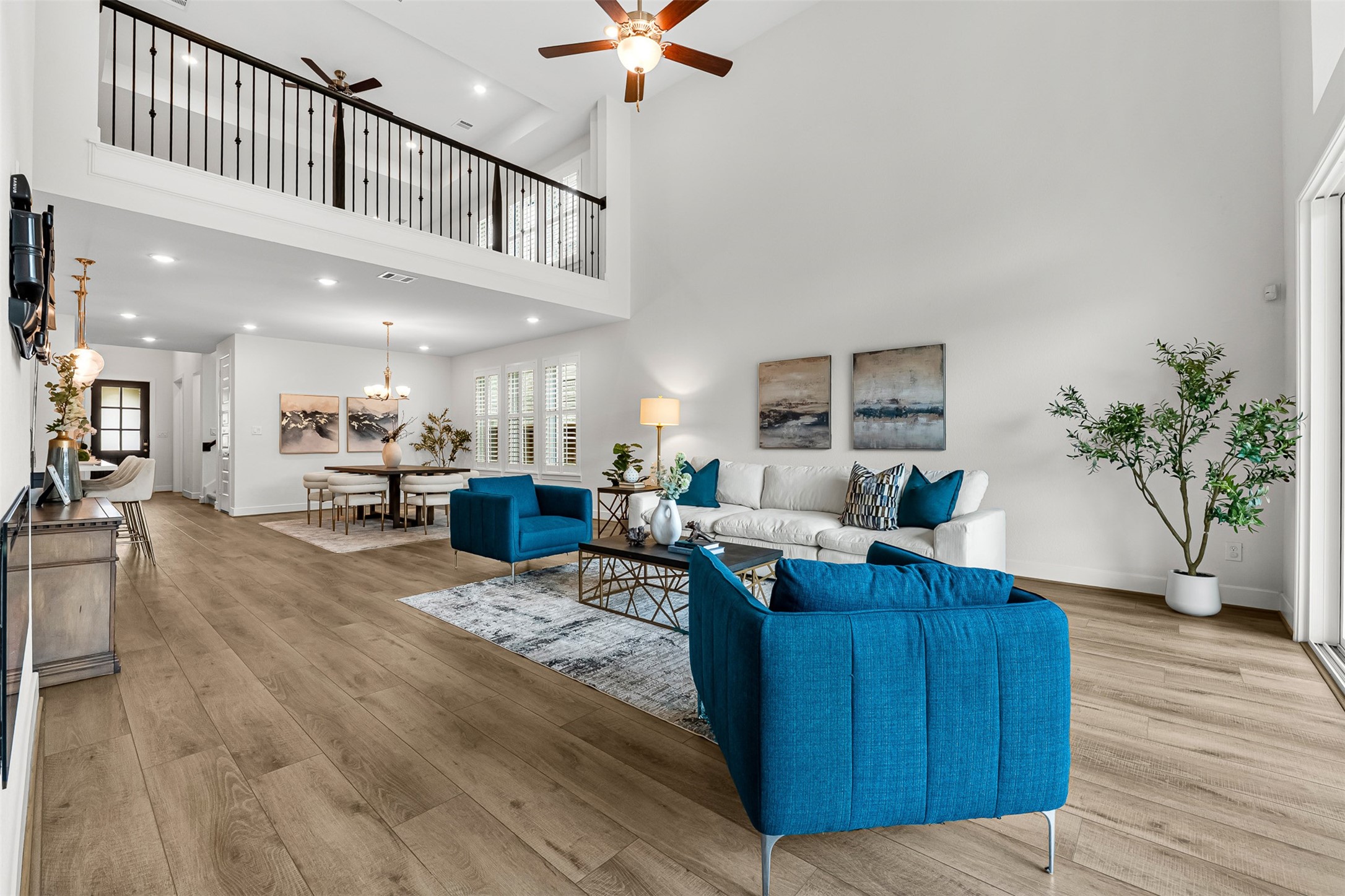 Soaring double-height ceilings and a dramatic second-floor overlook anchor this open-concept main living area. Wood-look flooring flows effortlessly toward the adjoining dining space, while expansive sliding glass doors provide direct patio access.
