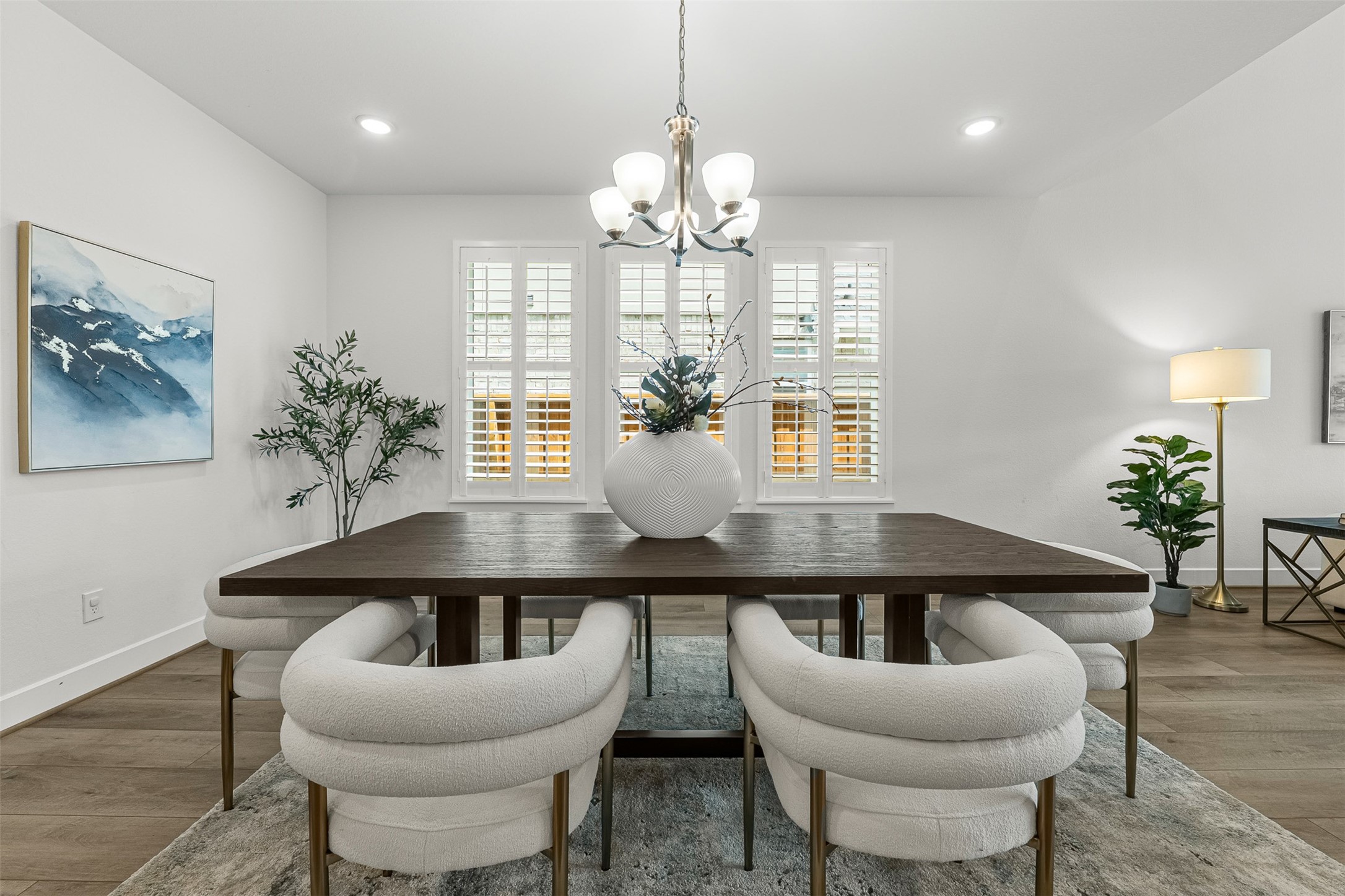 Elegant plantation shutters and a classic multi-light chandelier frame this spacious formal dining room with soft, ambient illumination. Open to the surrounding living spaces, the room easily accommodates a large dining table atop sleek wood-look flooring.
