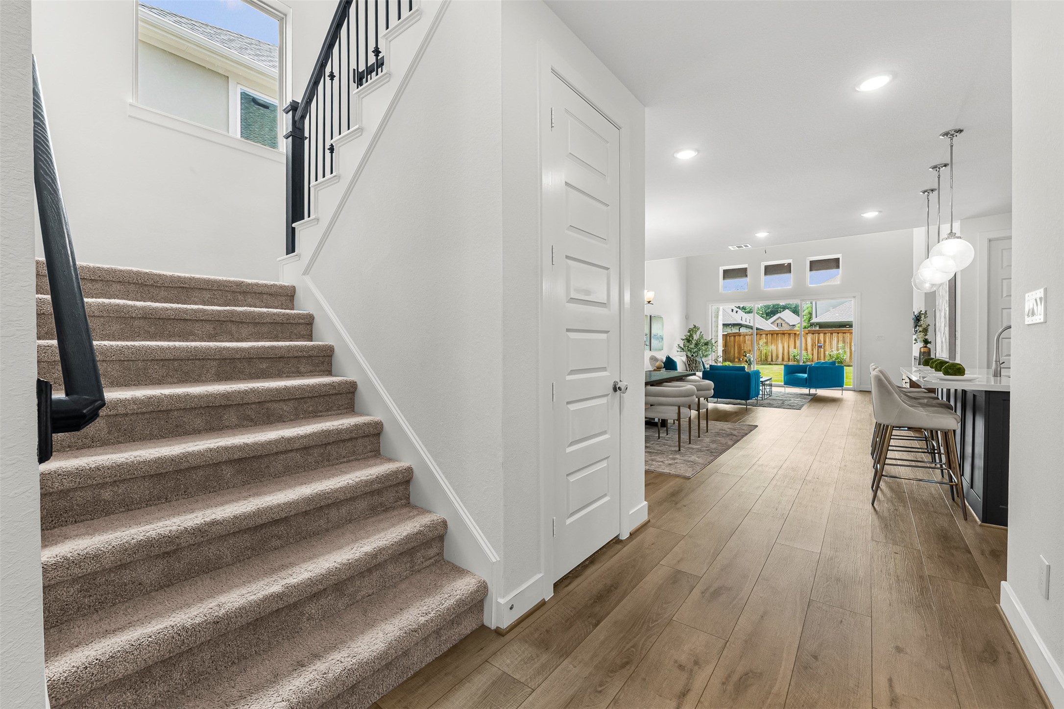 Plank flooring stretches from the entry hallway into the main floor living space, passing a carpeted staircase with wrought-iron balusters. A main-floor storage closet sits near the kitchen island, offering convenient organization steps from the central living area.