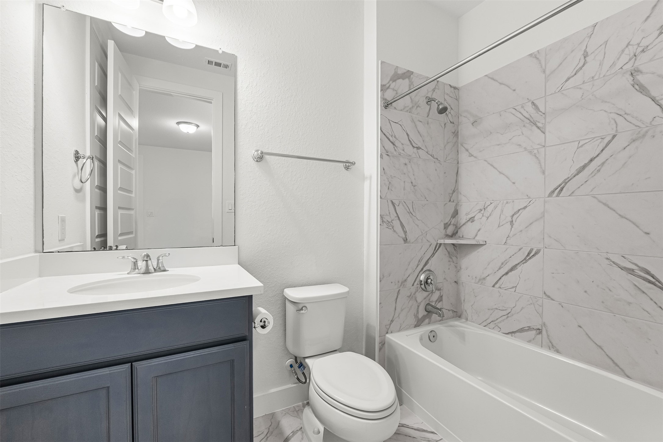 Contemporary navy vanity cabinetry pairs with crisp white quartz countertops and a sleek undersink basin in this full bathroom. Marble-inspired wall tile surrounds the tub-and-shower combination, adding a refined touch to the space.