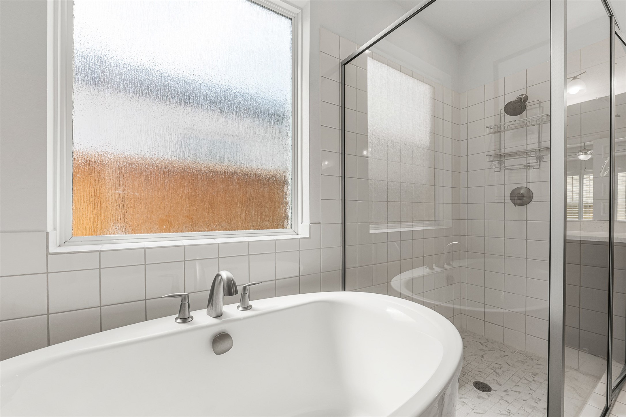A deep freestanding soaking tub and a sleek glass-enclosed shower with a marble-patterned tile floor create a spa-like retreat in this primary ensuite. Crisp white square wall tiles and textured privacy windows flood the space with soft light while maintaining complete seclusion.