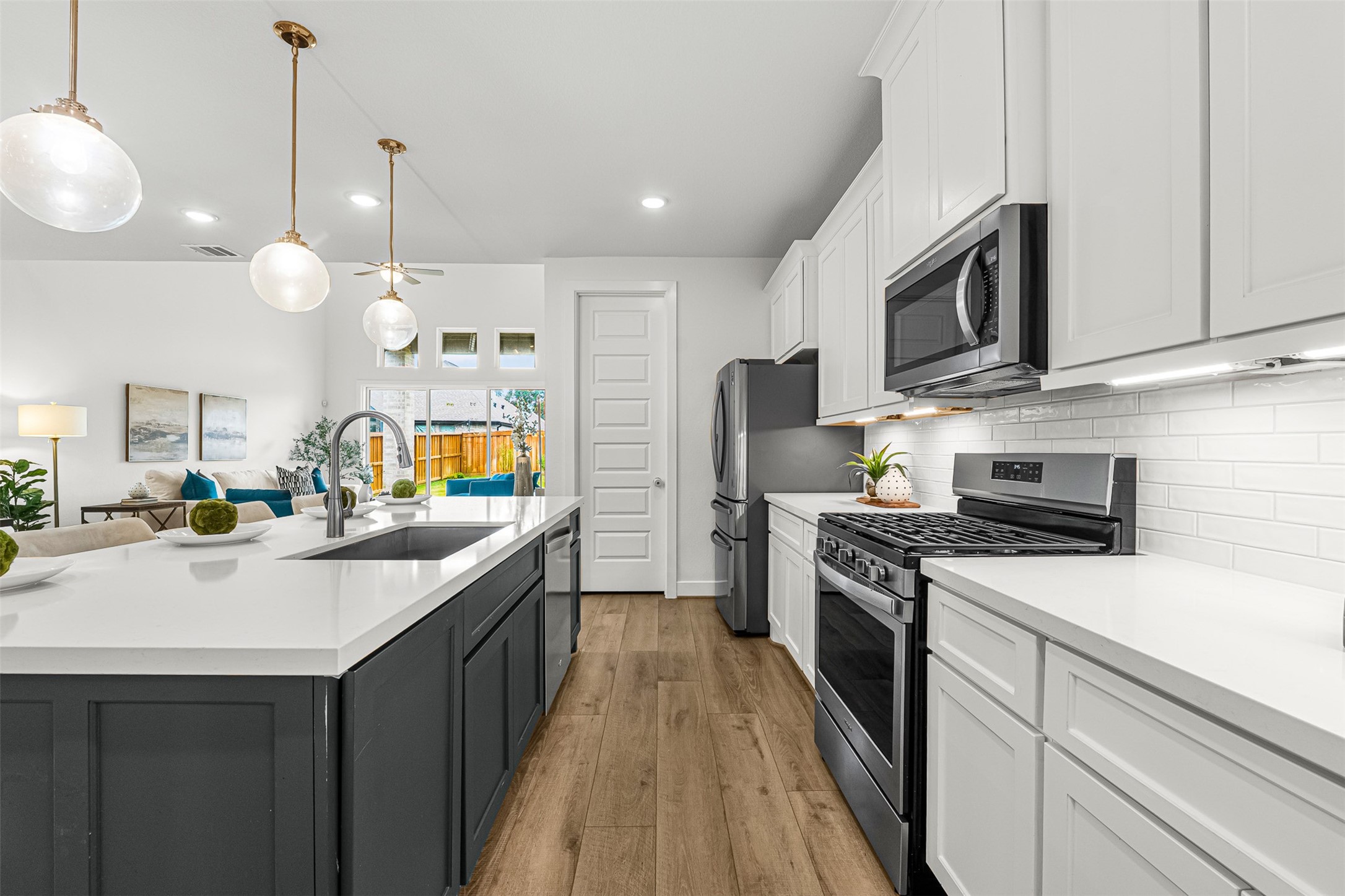 White quartz countertops pair with dark contrast island cabinetry and modern pendant lighting to create an inviting culinary centerpiece. Stainless steel appliances and a subway tile backsplash line the perimeter, offering an ideal layout for effortless meal preparation.