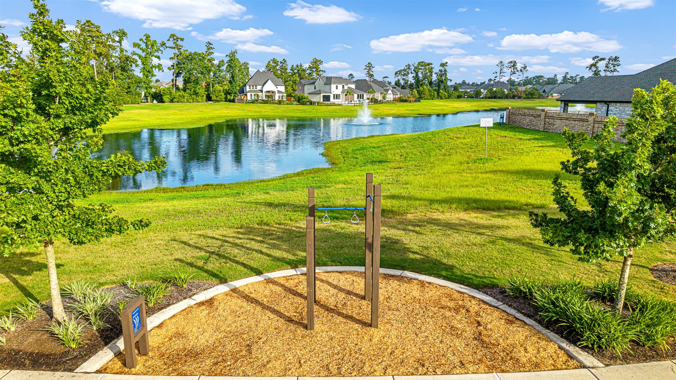An outdoor fitness station sits along a paved trail overlooking a tranquil catch-and-release pond with a fountain in this amenity-rich neighborhood.