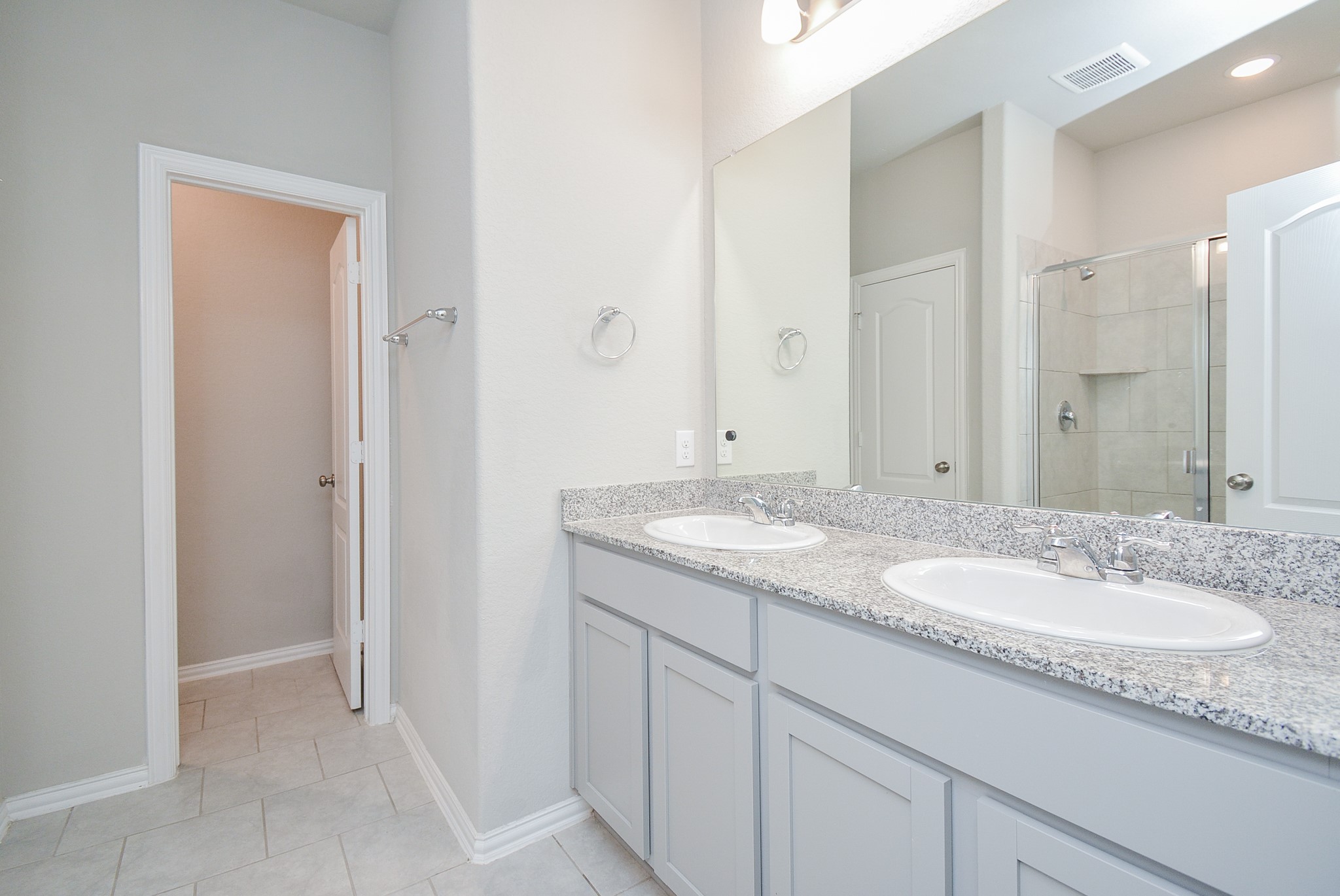 The primary ensuite bath offers a relaxing tone-on-tone theme, with double sinks, a sparkling wall-wide mirror and simple contemporary lighting above..