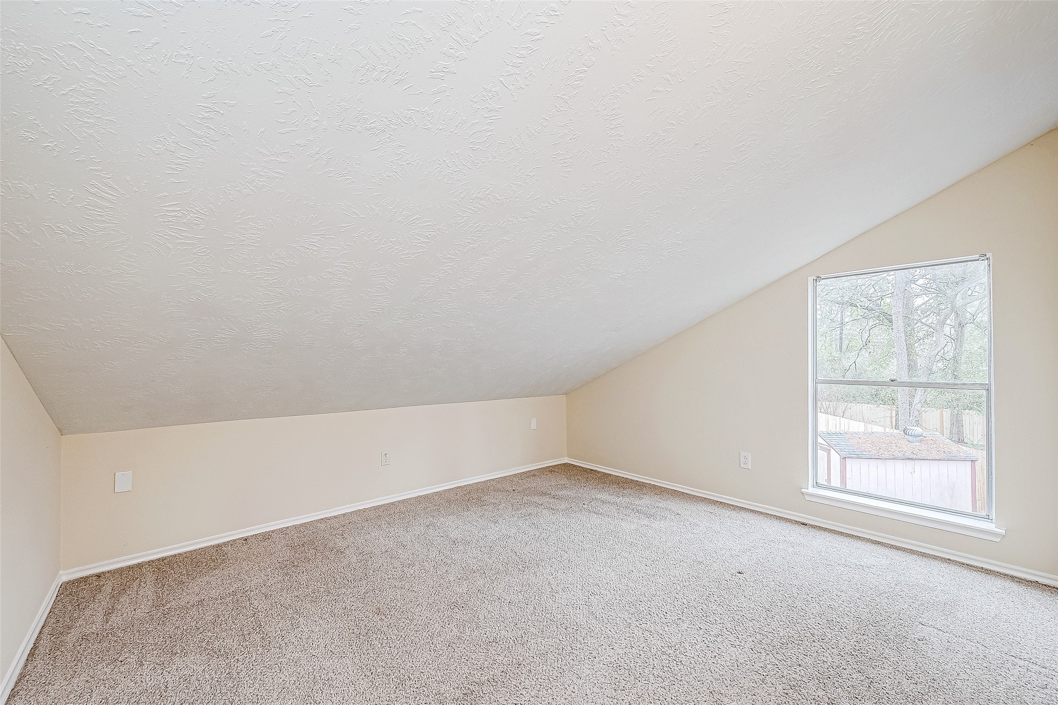 A flexible space with a sloping ceiling and a large window offers endless possibilities. Whether used as a study, playroom, or hobby area, this carpeted room adapts to your needs.