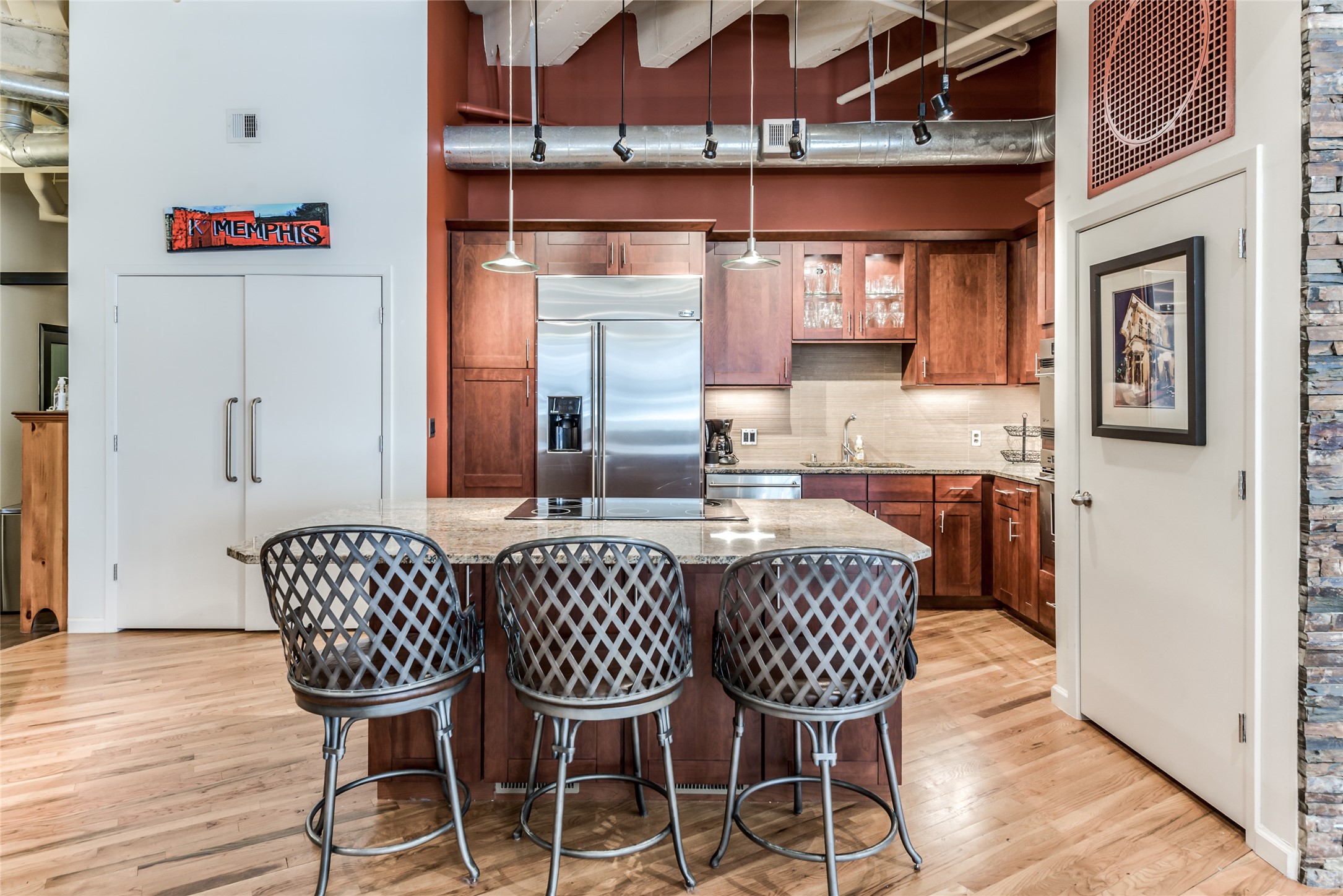 This kitchen features a modern industrial design with exposed ductwork and high ceilings. It includes a spacious island with granite countertops and seating.
