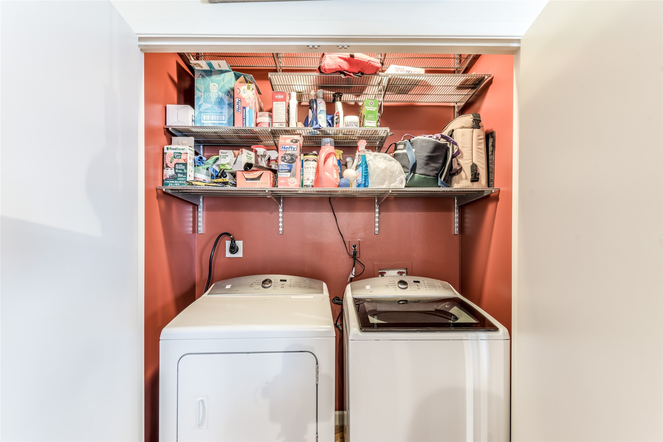 Compact laundry nook with a washer and dryer below two shelves stocked with various household supplies. Ideal for efficient use of space.