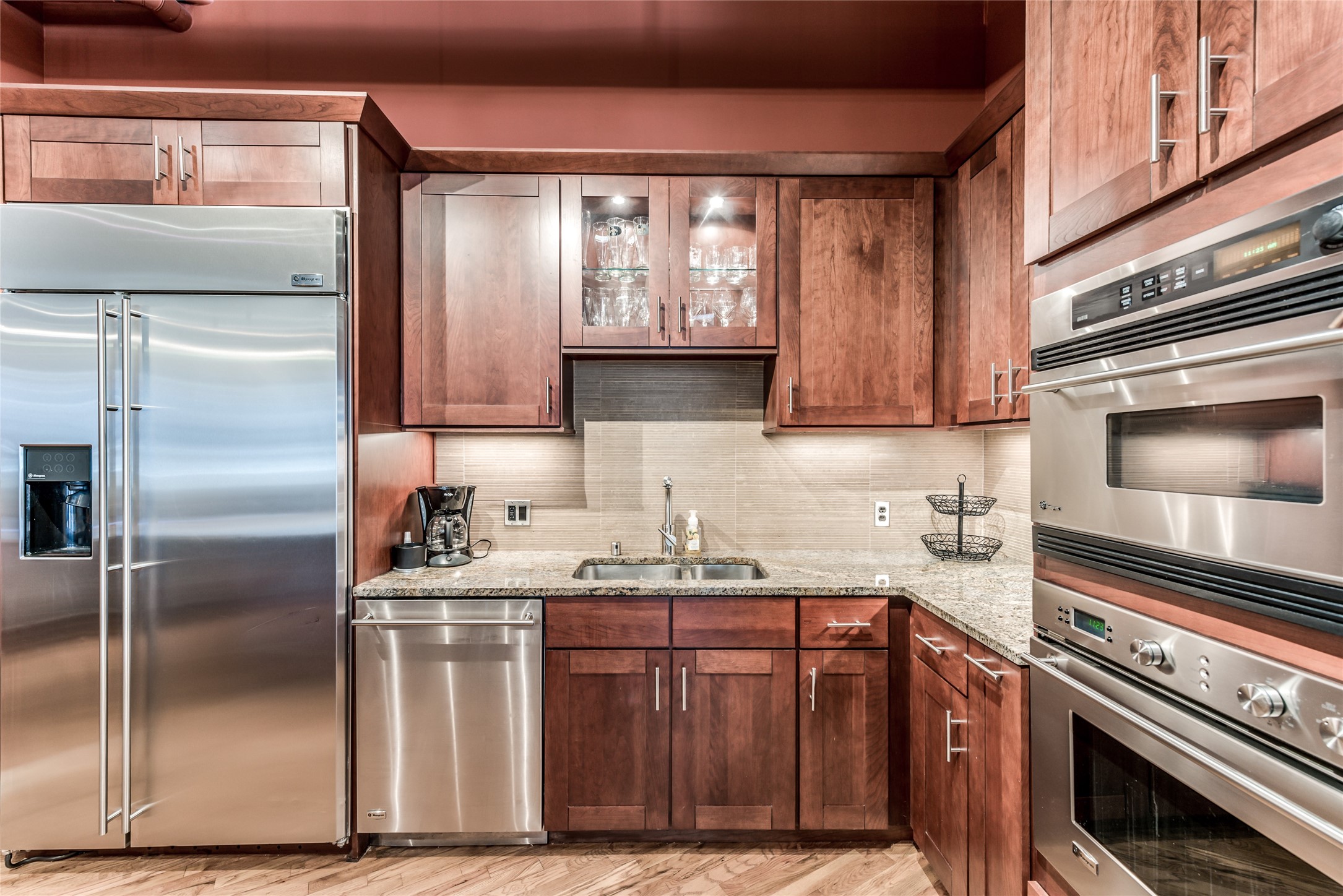 This kitchen features modern stainless steel appliances, including a double oven and a large fridge. It has rich wooden cabinetry, granite countertops, and a stylish tile backsplash, offering both functionality and elegance. This kitchen features modern stainless steel appliances, including a double oven and a large fridge. It has rich wooden cabinetry, granite countertops, and a stylish tile backsplash, offering both functionality and elegance.