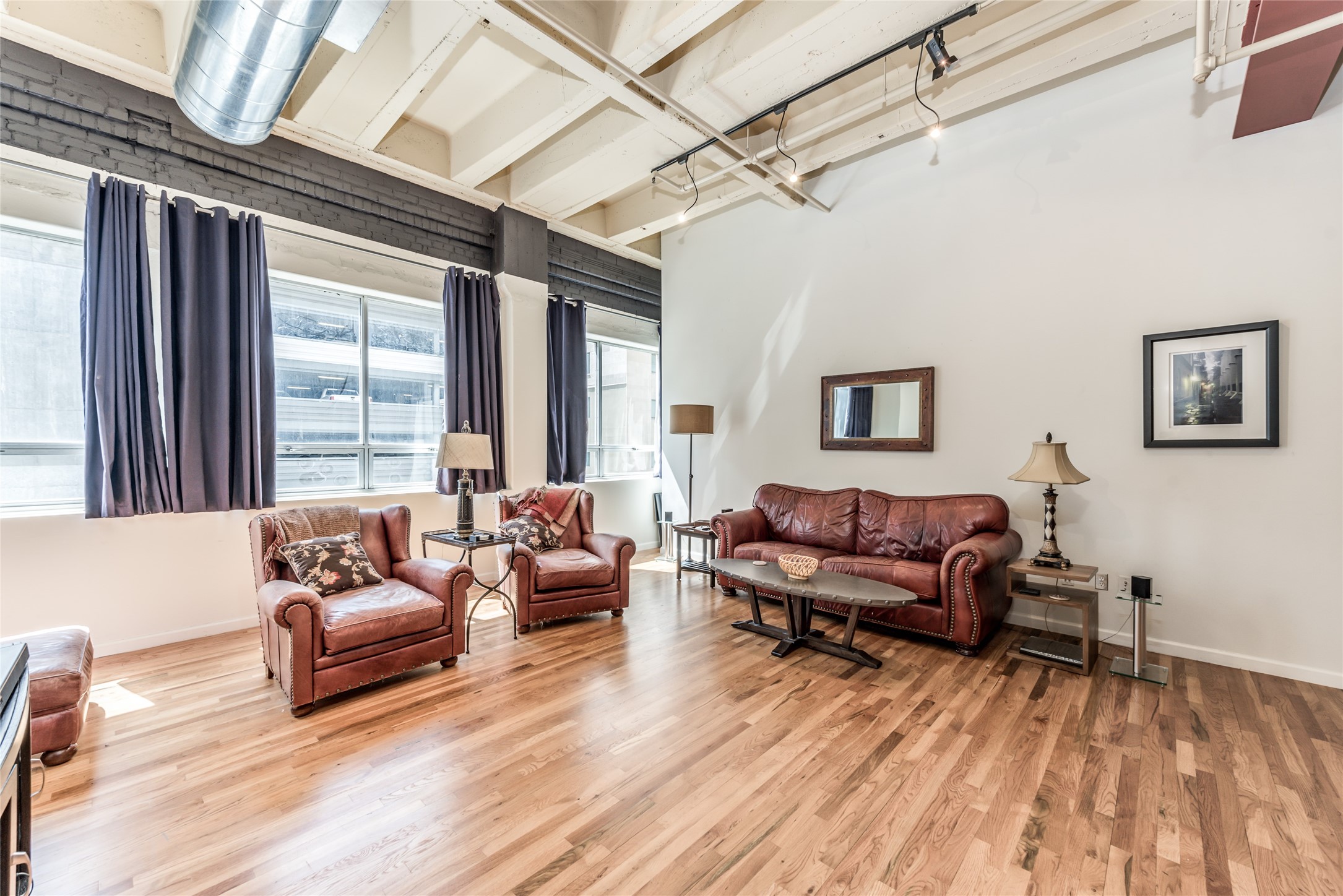 This spacious living room features a modern industrial vibe with exposed ductwork, high ceilings, and large windows for ample natural light. This spacious living room features a modern industrial vibe with exposed ductwork, high ceilings, and large windows for ample natural light.