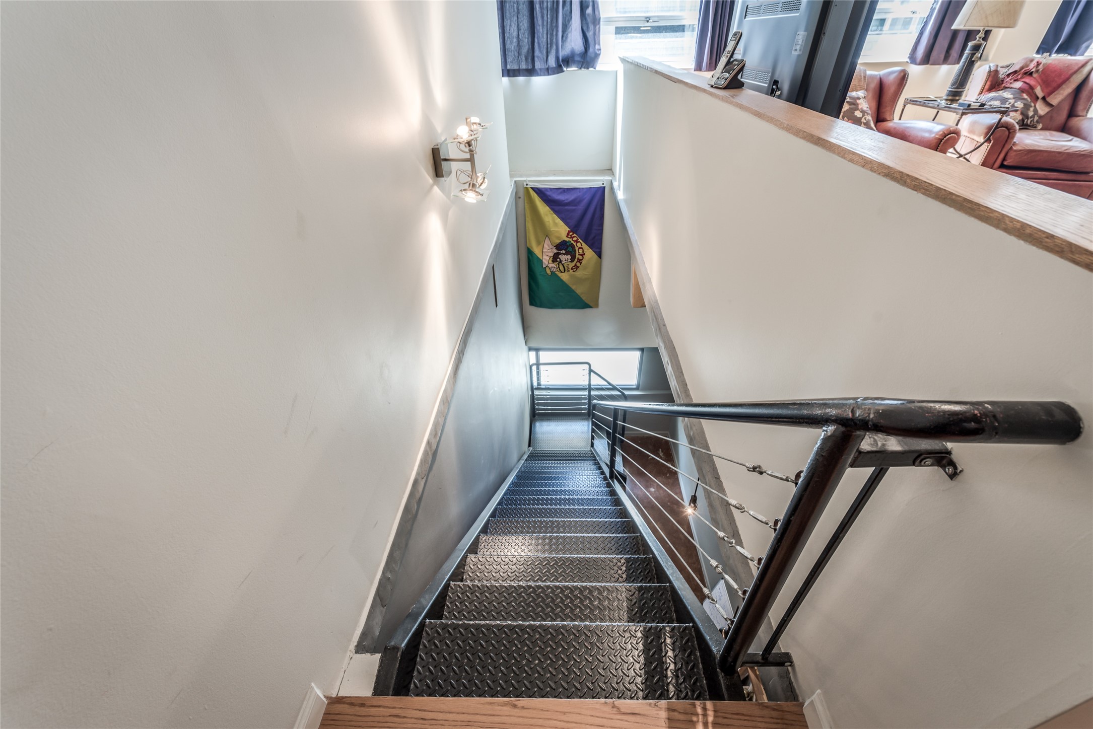 This photo showcases a modern staircase with metal steps and a sleek railing, leading to lower level area to primary bedroom with natural light from large windows.