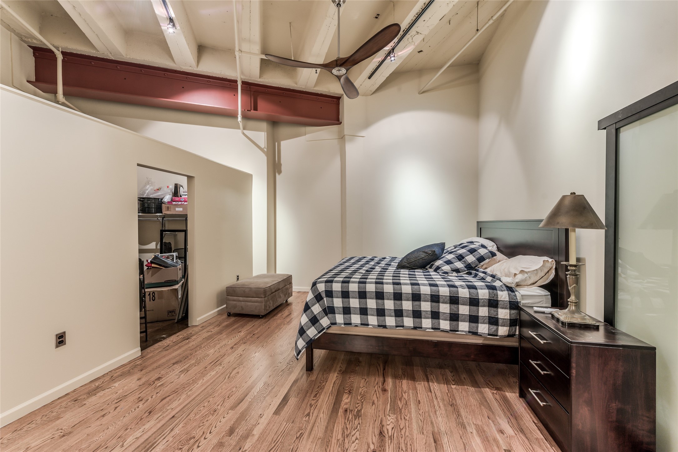 This photo features a bedroom with a modern industrial vibe, highlighted by exposed beams and a ceiling fan.