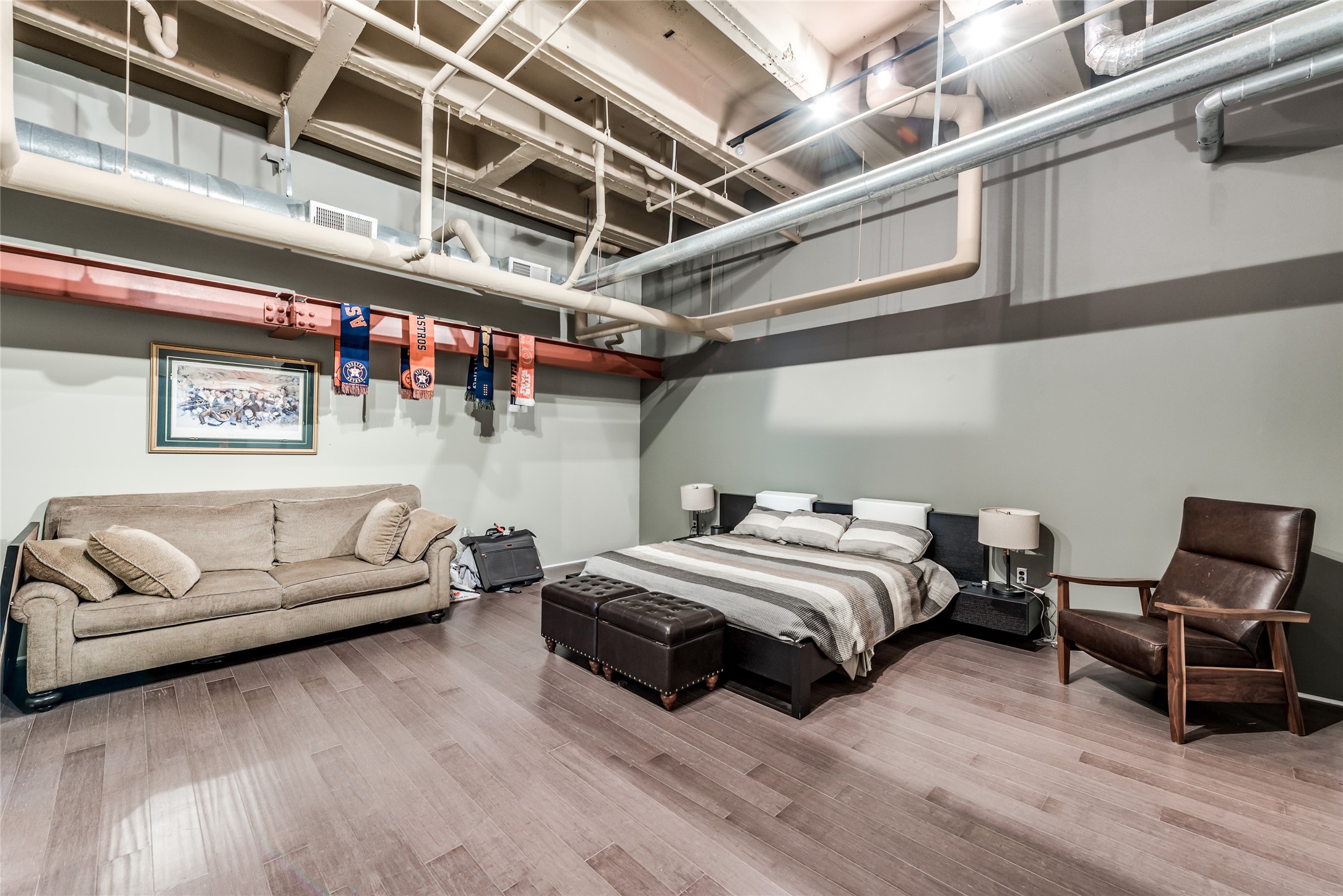 This loft-style primary bedroom features exposed ductwork and beams for an industrial feel.