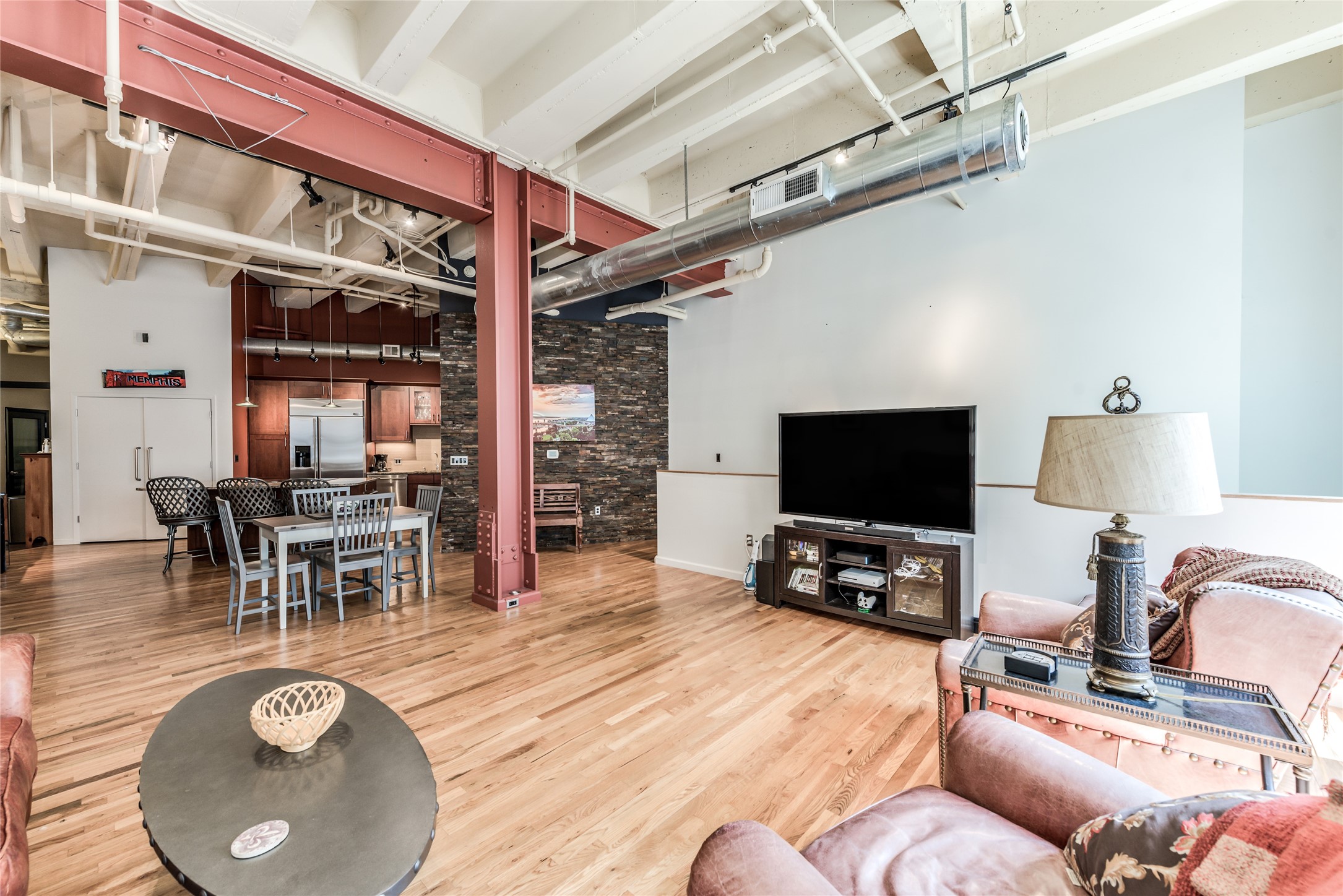 This open-concept loft features high ceilings with exposed beams and ductwork, hardwood floors, and a mix of industrial and rustic elements.