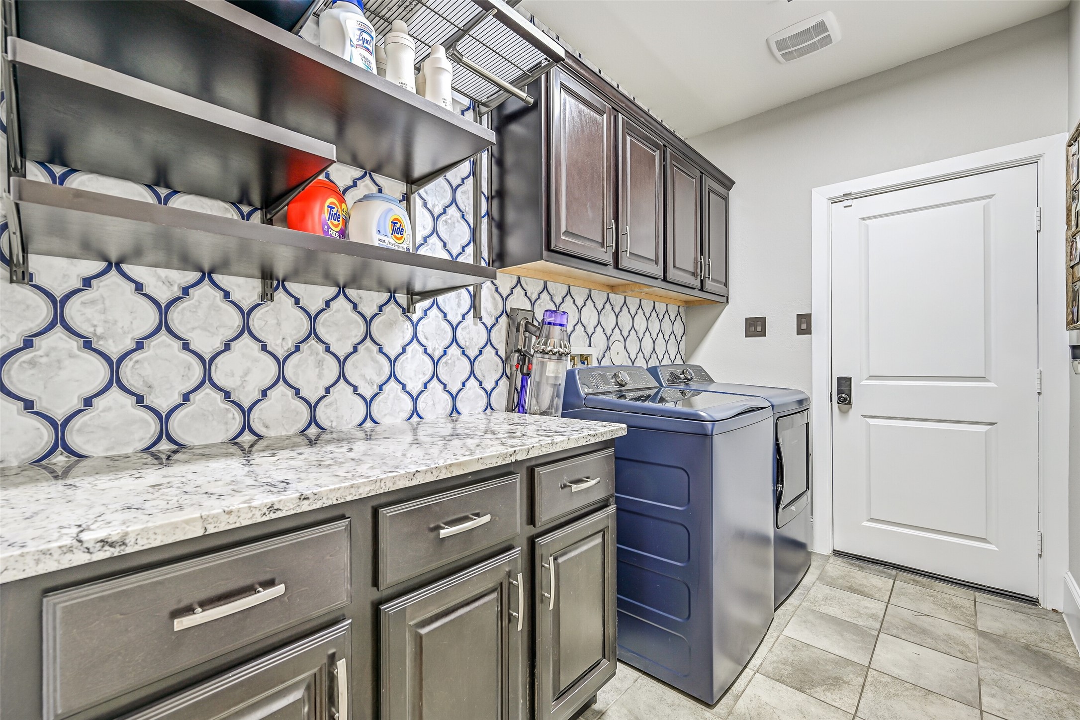 The customized utility room offers a granite folding station, extensive cabinetry, adjustable open shelving and a decorative full-height tile treatment. Washer & dryer are included, and the adjoining door provides direct access to the 3-car garage.