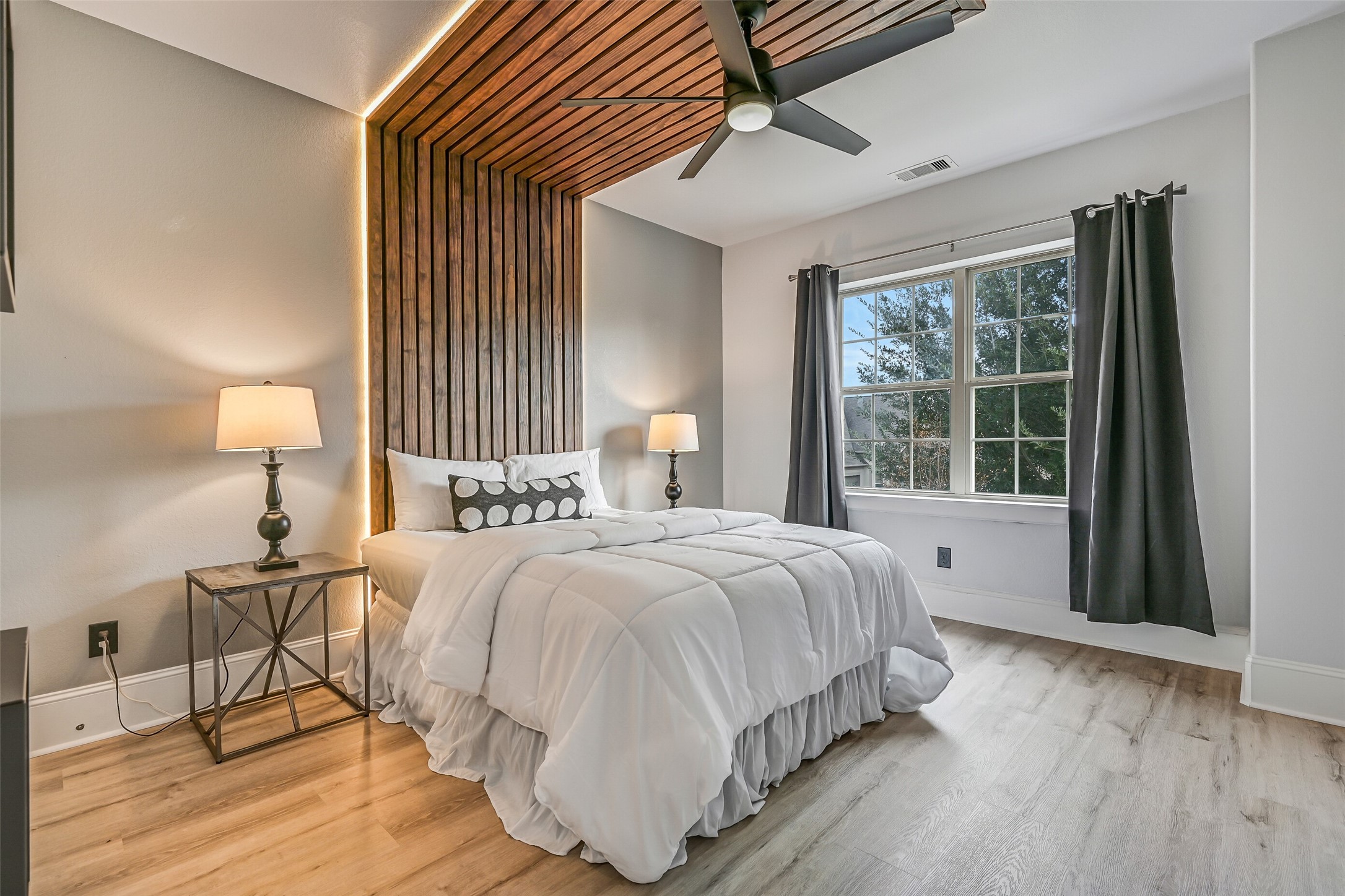 One of four upstairs secondary bedrooms, this inviting room features LVP flooring, a dramatic wood-slat wall and ceiling treatment with integrated accent lighting, modern ceiling fan and front-facing windows.