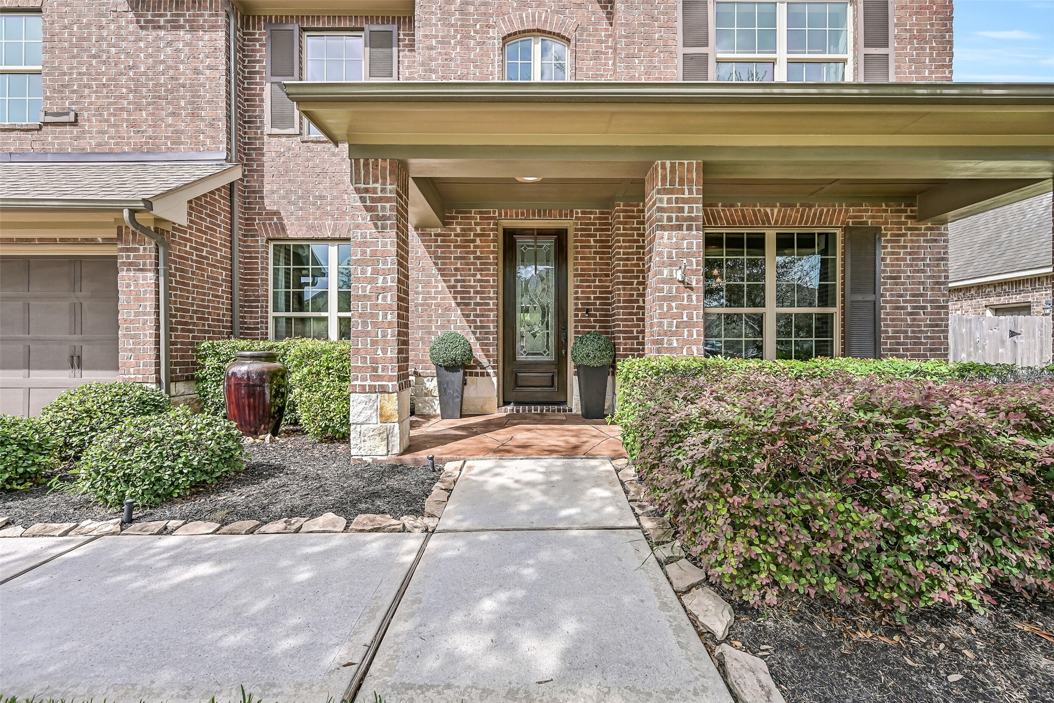 A welcoming covered front porch leads to the decorative glass entry door, surrounded by neatly maintained landscaping. In-ground irrigation helps keep the lawn and landscaping looking their best.