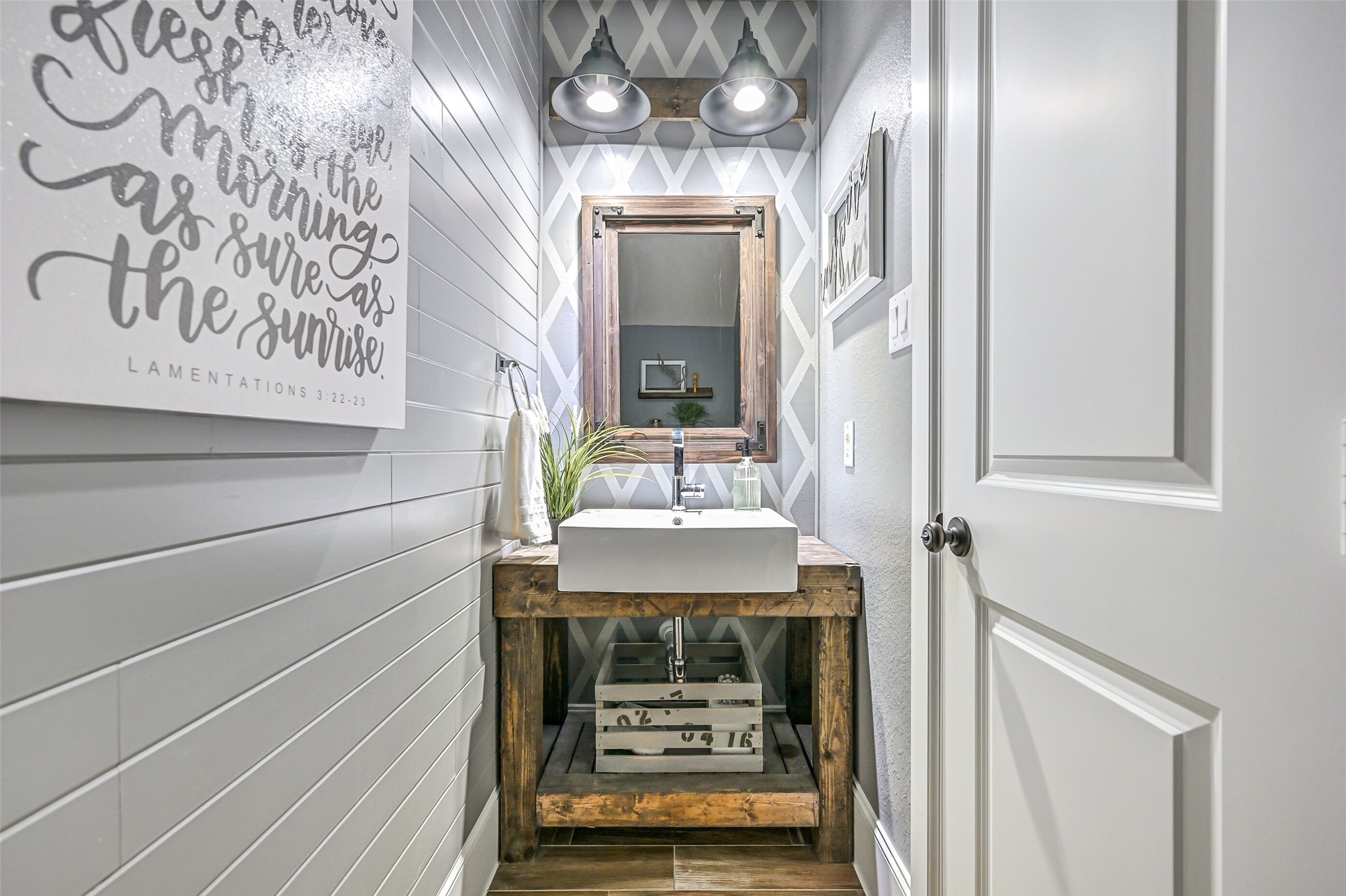 Tucked into a convenient alcove off the family room, this stylish powder bath features shiplap, a geometric accent wall, rustic wood vanity with vessel sink, industrial-style lighting & coordinating framed mirror.