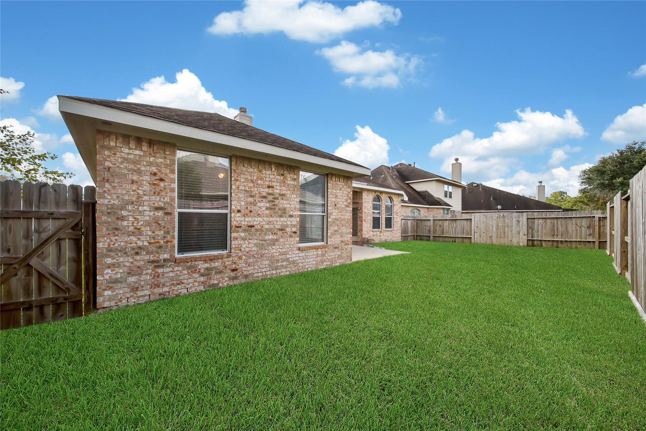This is a single-story brick home with a back lawn and a privacy fence, featuring a spacious backyard and a clear sky above.