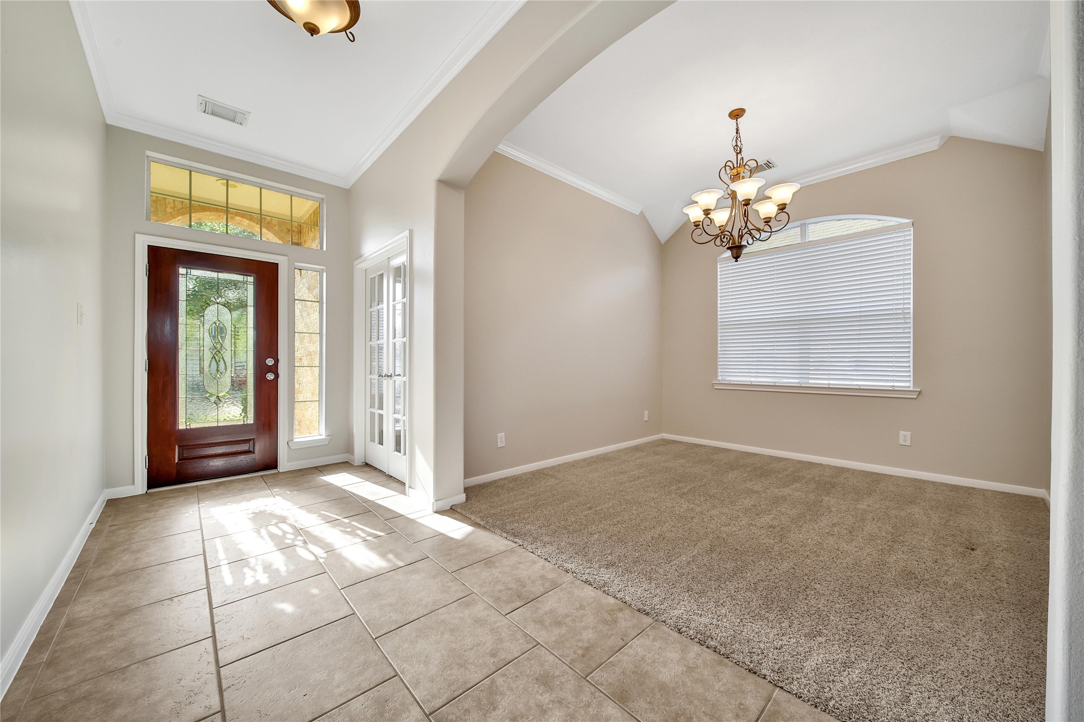 This bright foyer features a solid wooden door with decorative glass and a sidelight. Natural light streams through the transom and large window, fitted with blinds, and there's an adjacent study with french doors and an elegant dining room which could also be used as a game room or flex space.