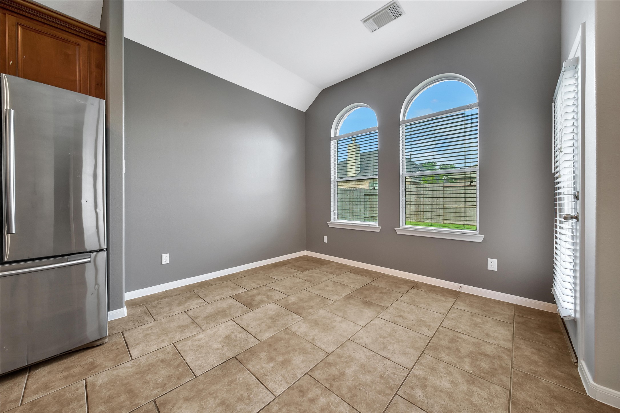 This is a bright, breakfast room open to the kitchen and living room, neutral gray walls, and two large arched windows that let in plenty of natural light. Enjoy views of the backyard through the arched windows.