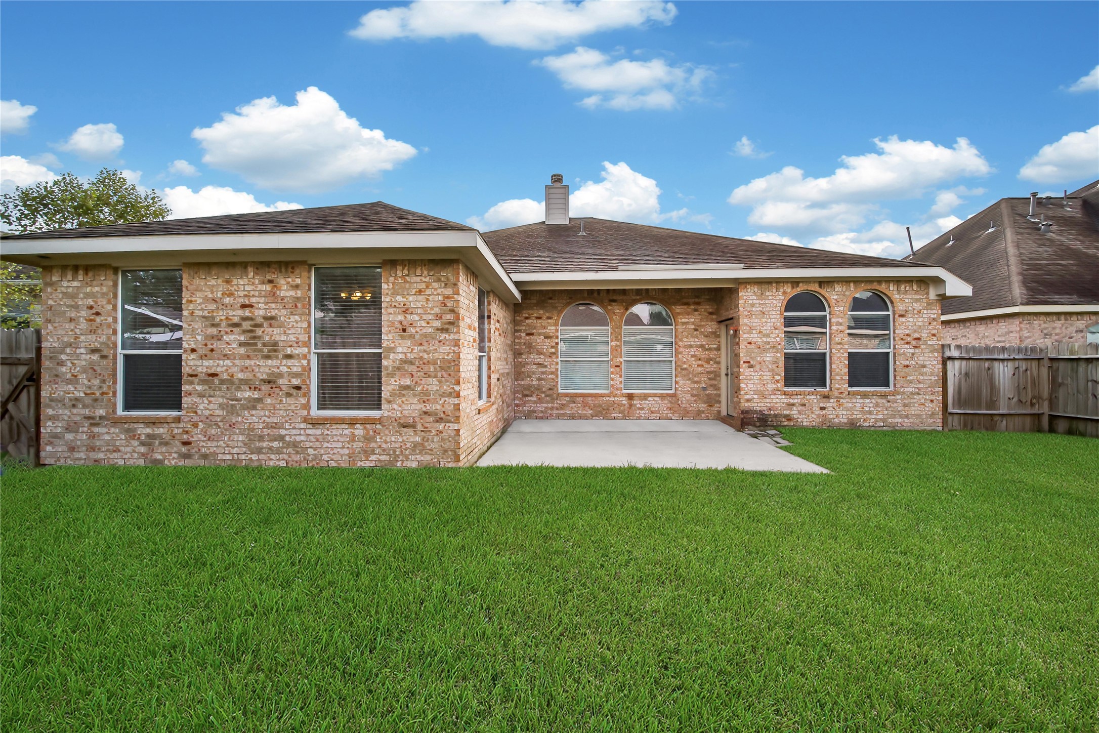 This is a single-story brick home featuring a back lawn and a concrete patio area in the backyard, with a privacy fence surrounding the property.