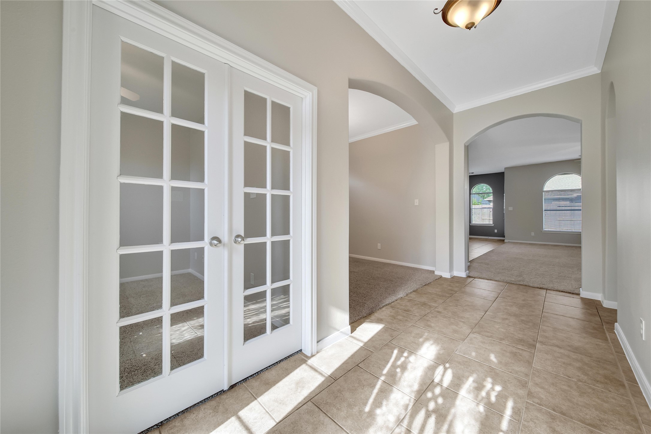 This bright foyer features a solid wooden door with decorative glass and a sidelight. Natural light streams through the transom and large window, fitted with blinds, and there's an adjacent study/flex room with french doors and an elegant dining room which could also be used as a game room or flex space.