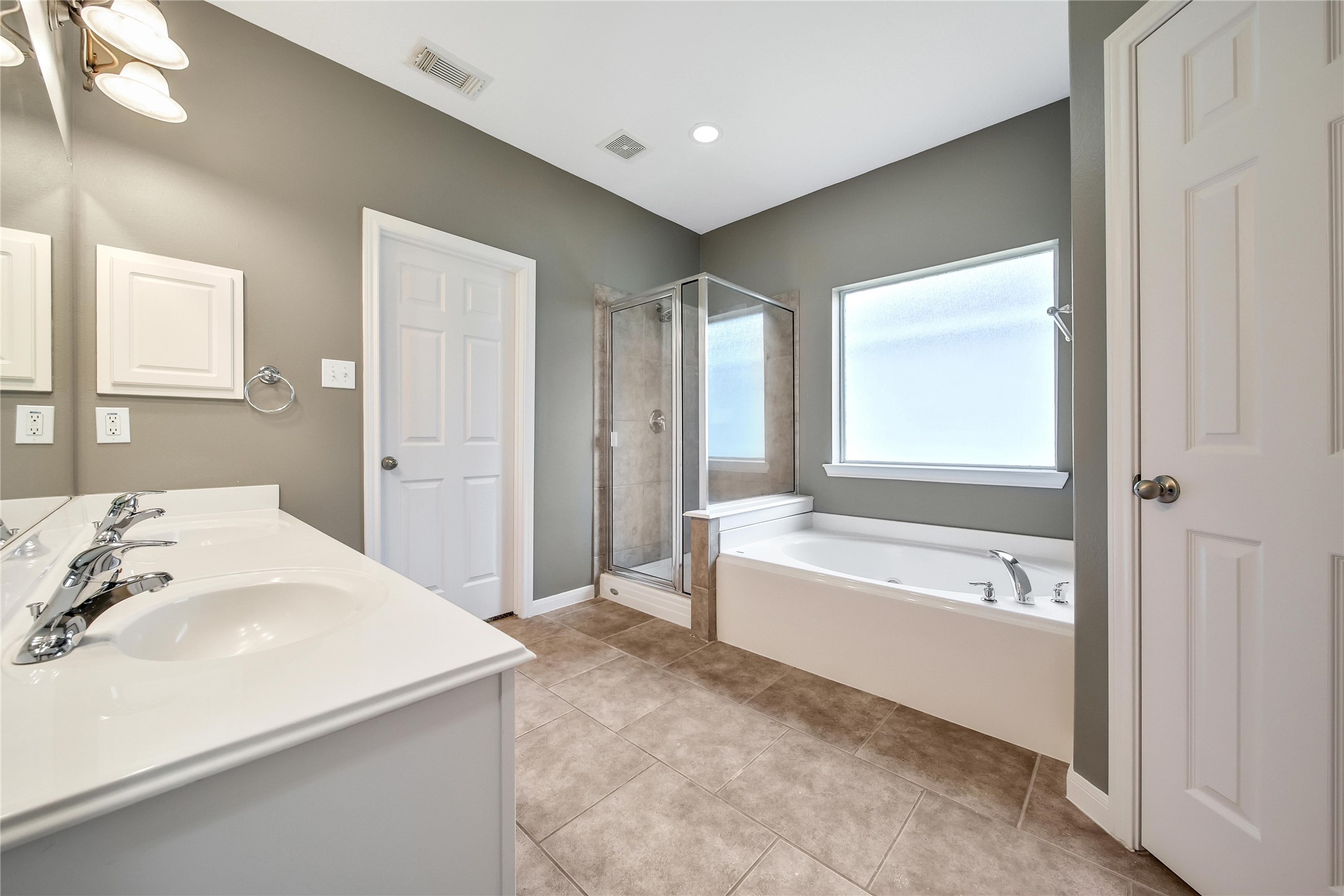 The modern looking primary bathroom features an oversized glass-enclosed shower, a separate bathtub, tiled flooring, and neutral wall colors. It includes a window for natural light, and a huge closet.