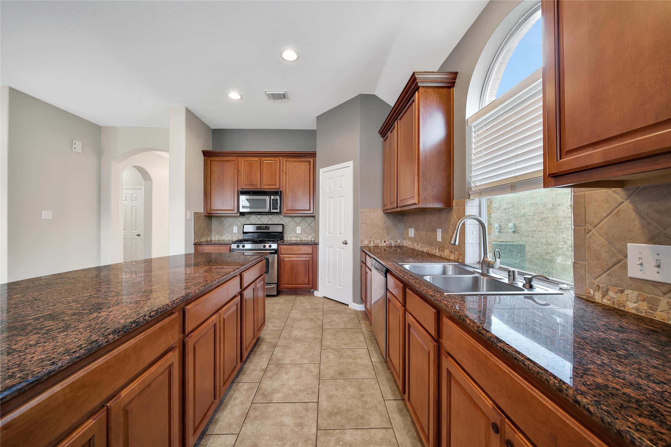 This is a spacious, well-lit kitchen with rich wooden cabinetry and granite countertops, featuring modern appliances and a large window over the sink.