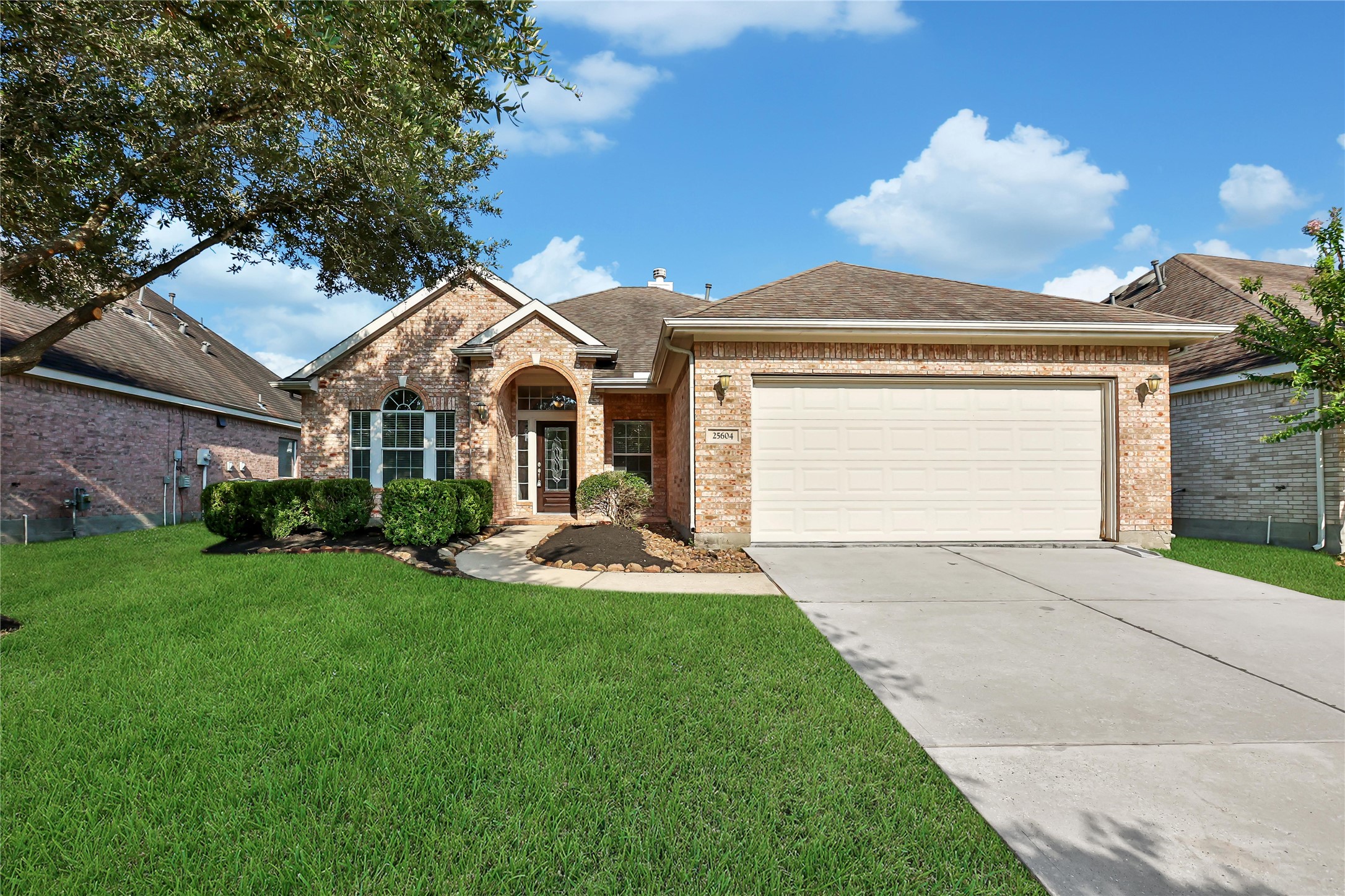 This is a well-maintained single-story brick home featuring a two-car garage, a mature oak tree in the front yard, and neat landscaping.