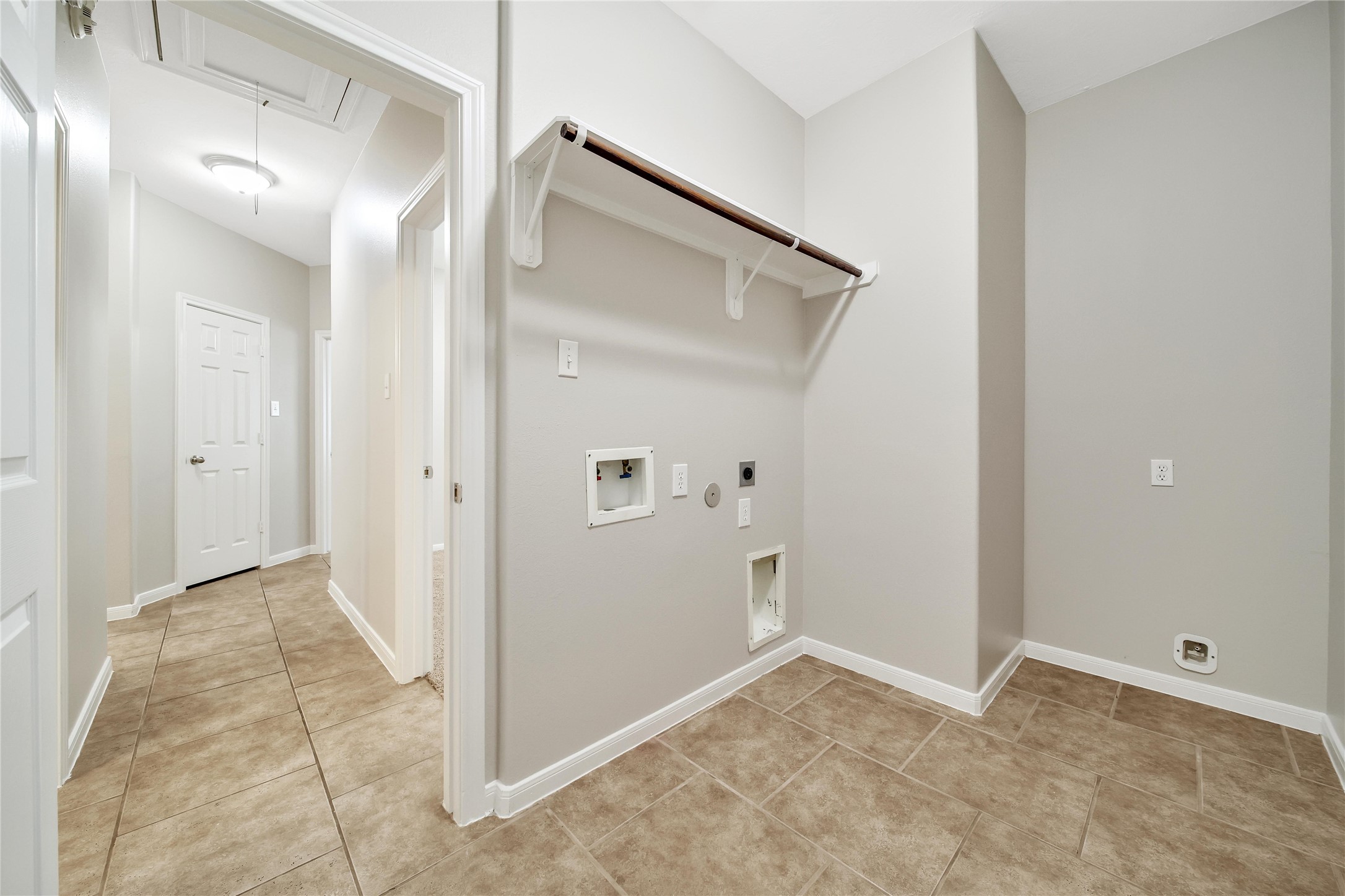 Spacious laundry room with hanging rack and room for a second fridge is located at the end of the split plan hall and has access to the garage.