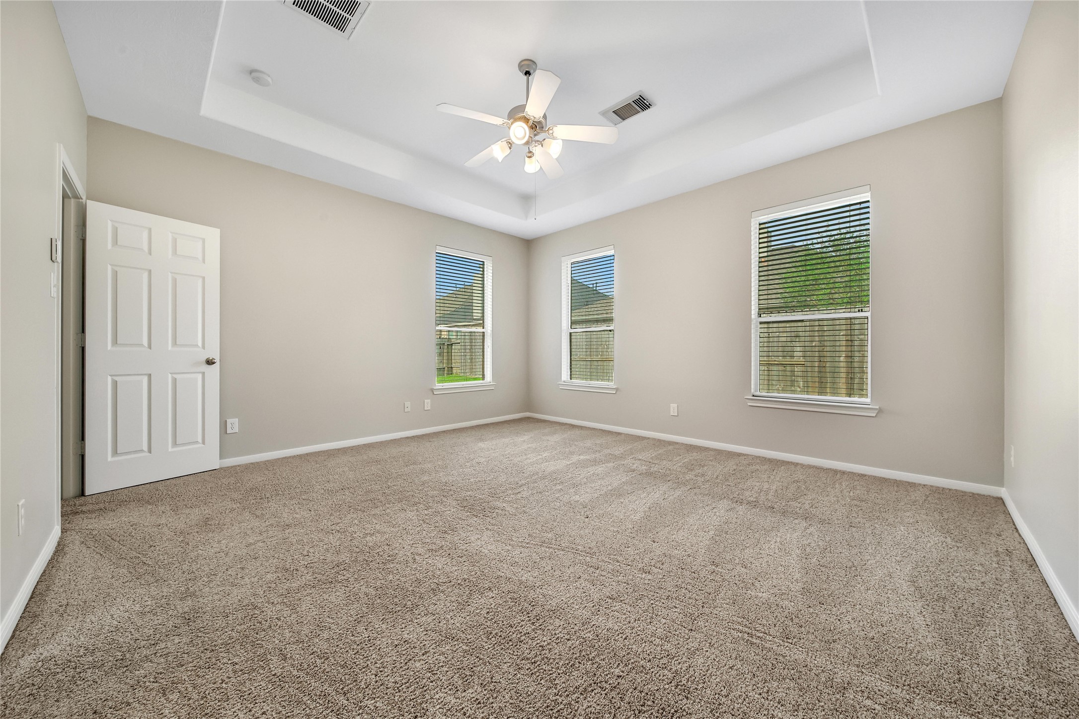 This is a spacious, well-lit Primary Bedroom with neutral walls, carpeting, and a ceiling fan with lighting. It features two large windows that allow for ample natural light.