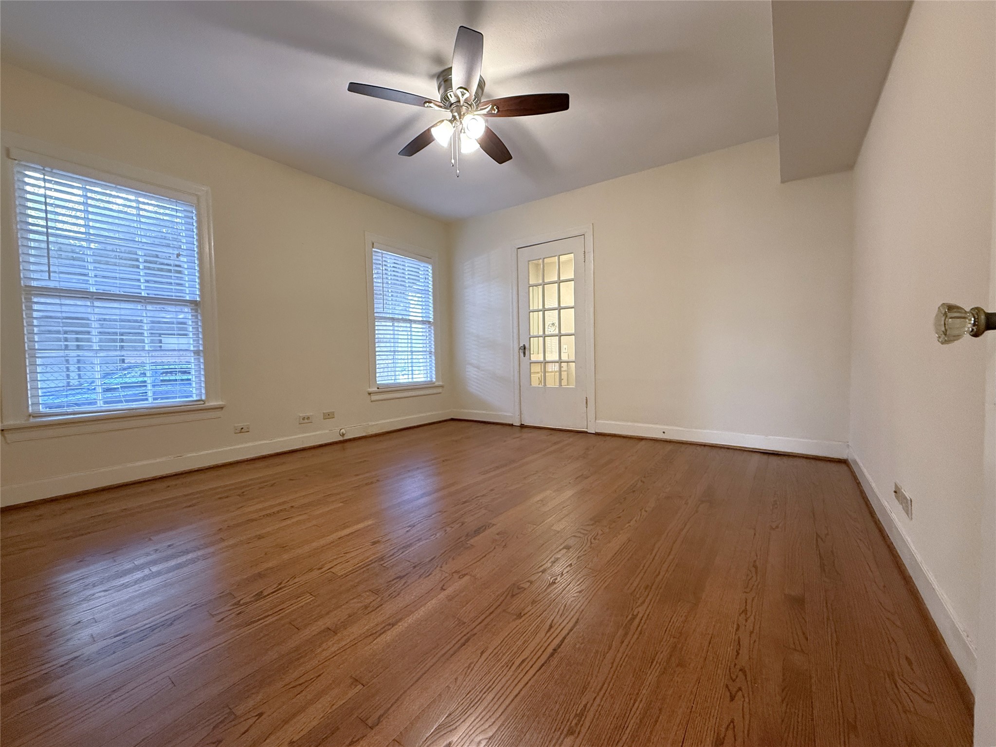 The primary bedroom with ceiling fan. Beyond the glass paned door is the primary bathroom. On the far right, notice the vintage glass door knob.